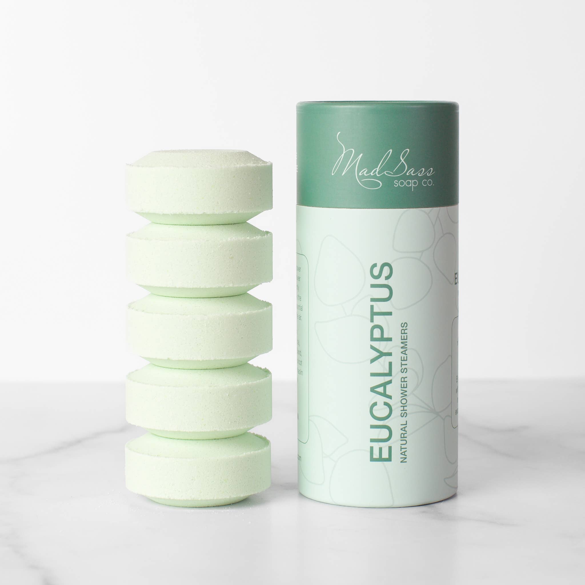 Stacked green eucalyptus shower steamer tablets next to packaging 