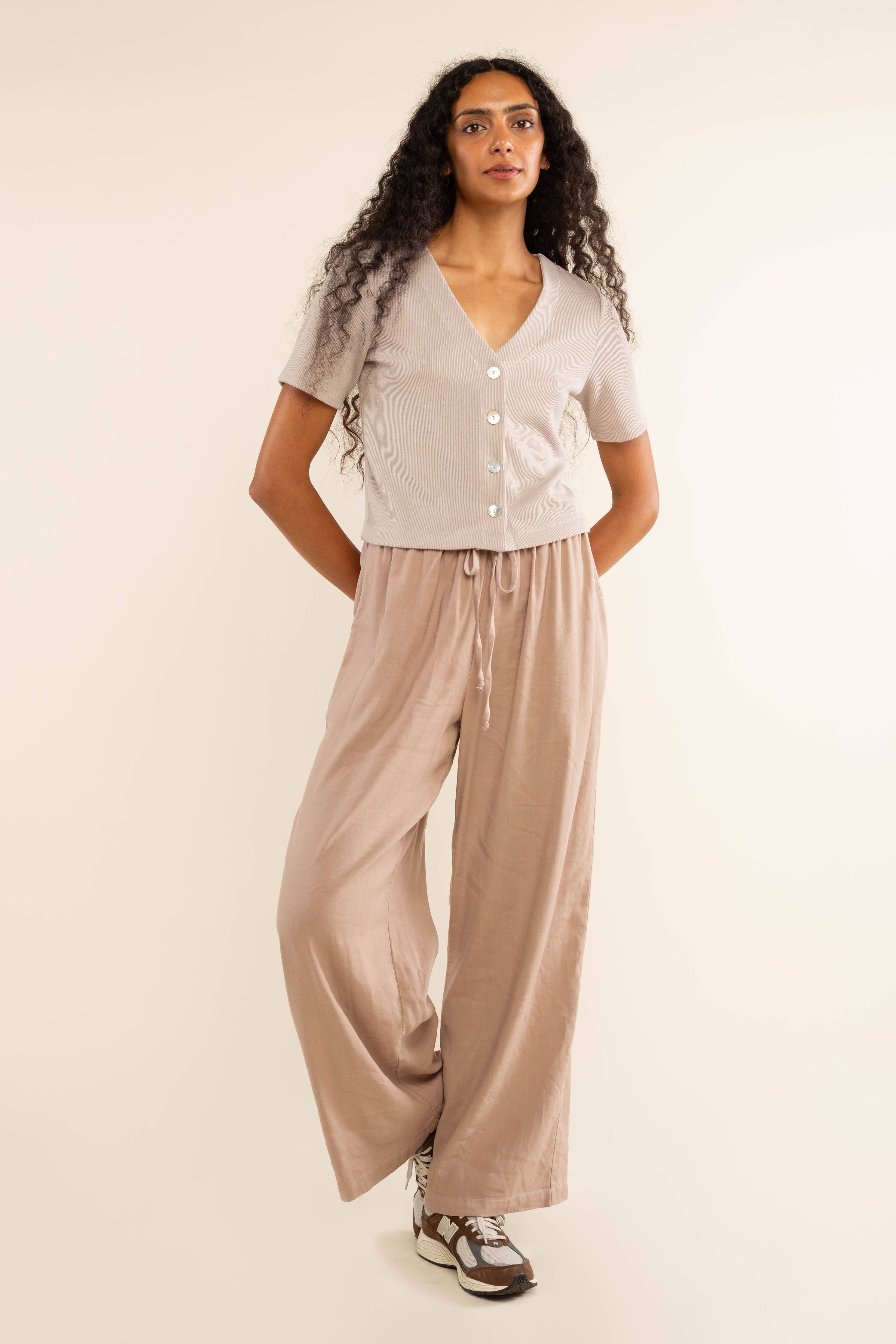 Woman wearing oat colored, ribbed, button down, short sleeve blouse top and beige pants 