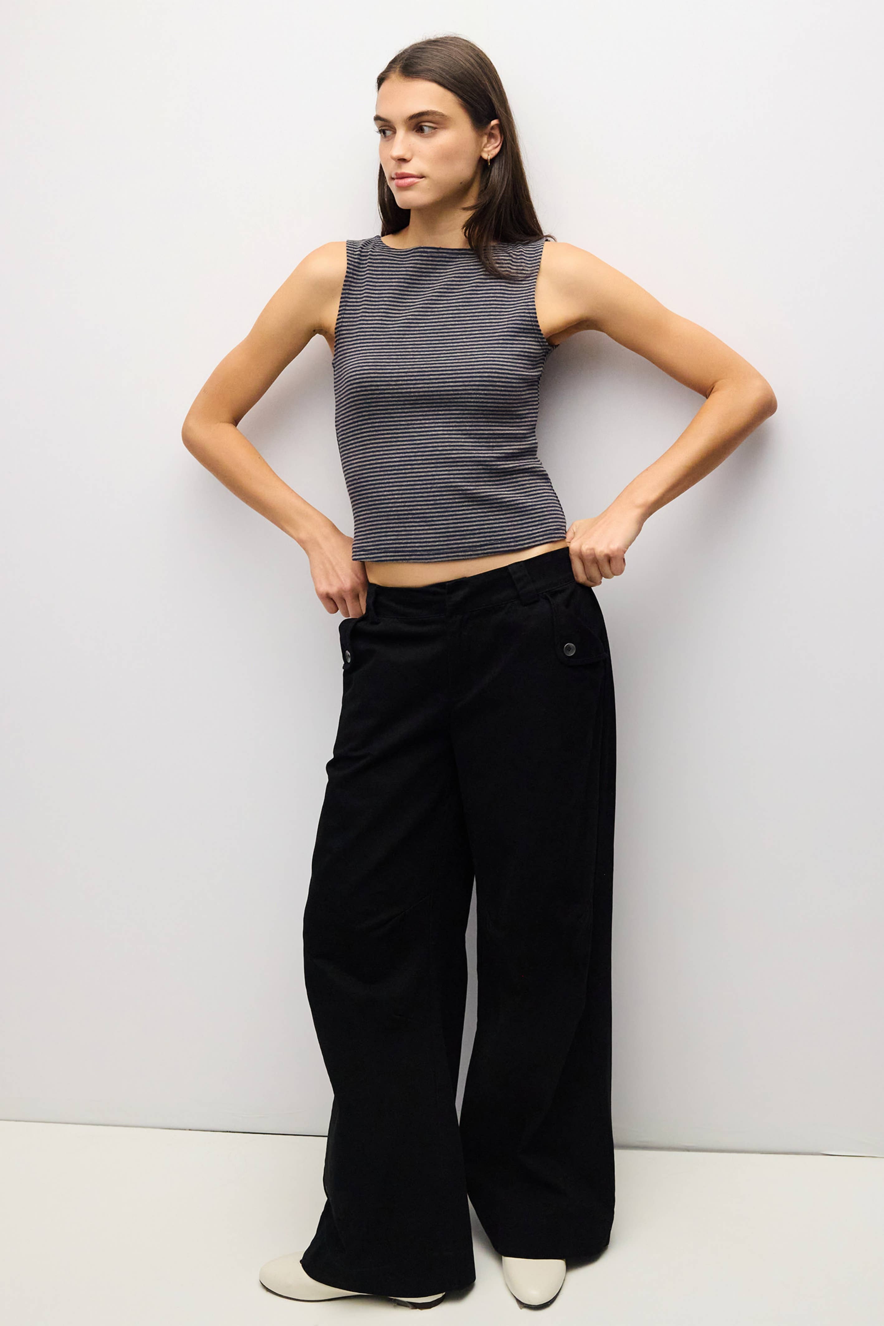 A woman modeling a sleeveless dark gray ribbed crop top and black wide-leg pants against a plain light gray studio background.