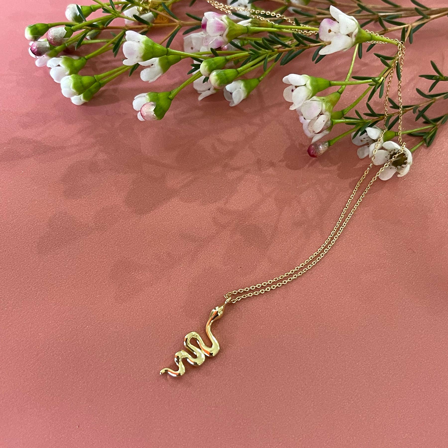 A gold necklace on a pink surface | Snake necklace pendant - FORM + CONTENT