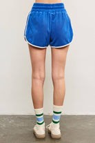 Woman wearing tube socks, tennis shoes, and electric marine blue terry cloth towel shorts with white lining details and white drawstring with hand in pocket 