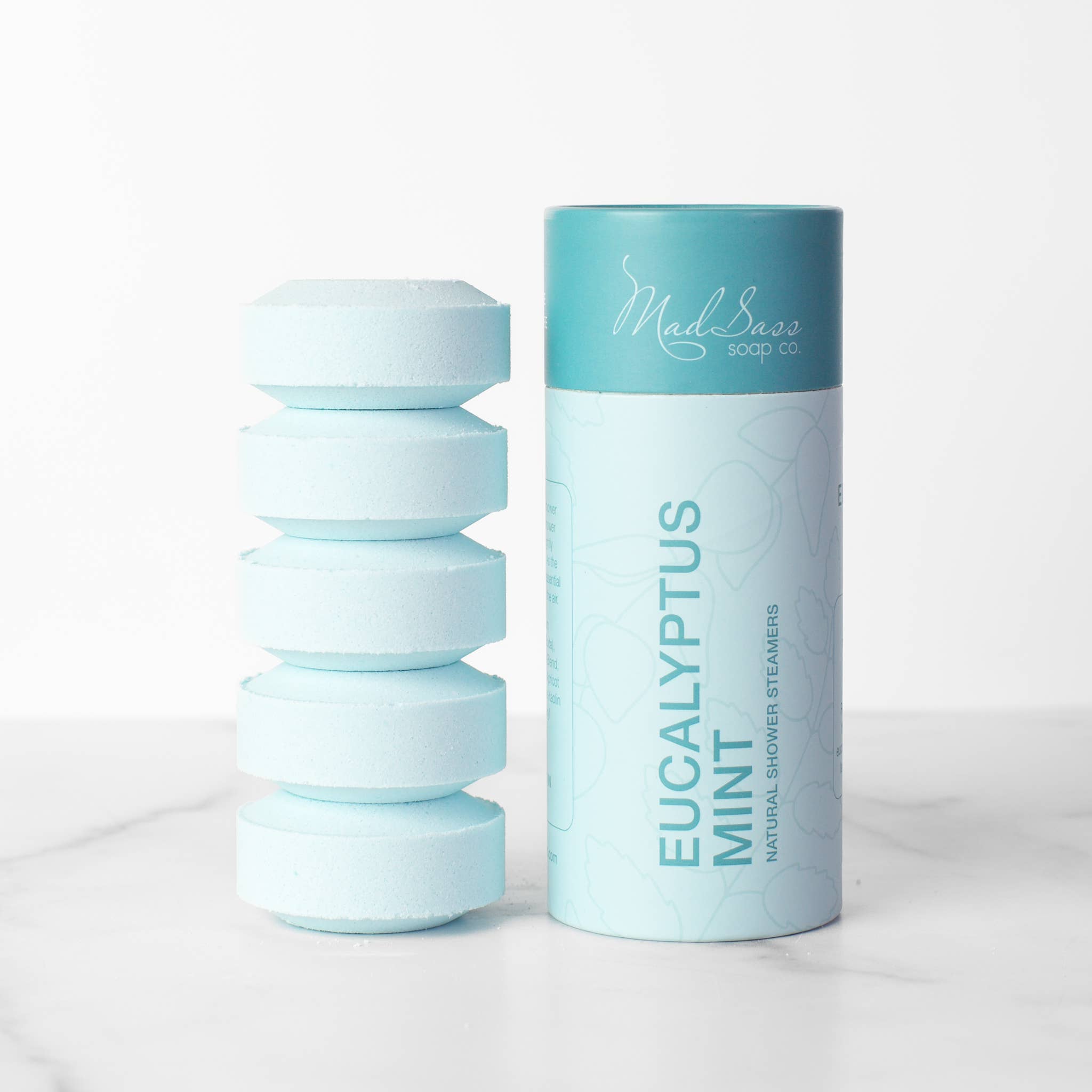 Stacked blue eucalyptus mint shower steamer tablets next to packaging 