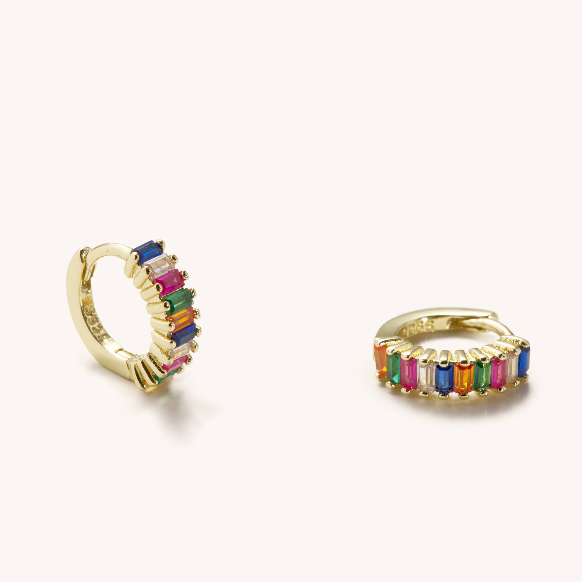 Small sized rainbow gem huggie earrings laying against a white background 