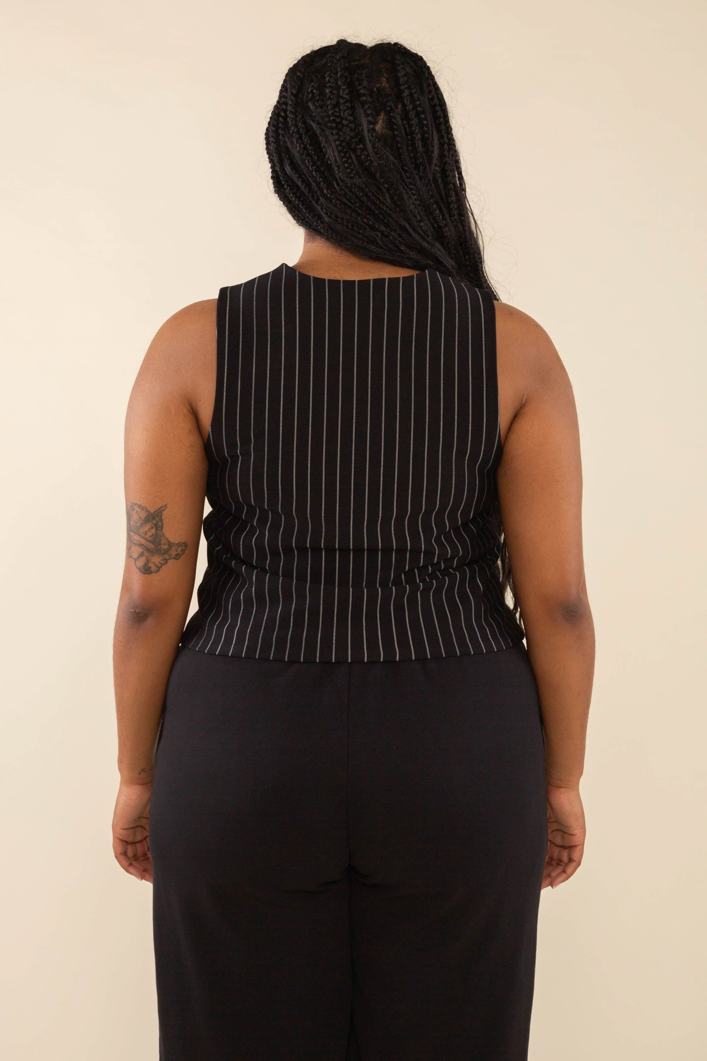 Woman turned away from the camera wearing black high neck vest with cream pinstripes. Vest has black buttons all the way down 