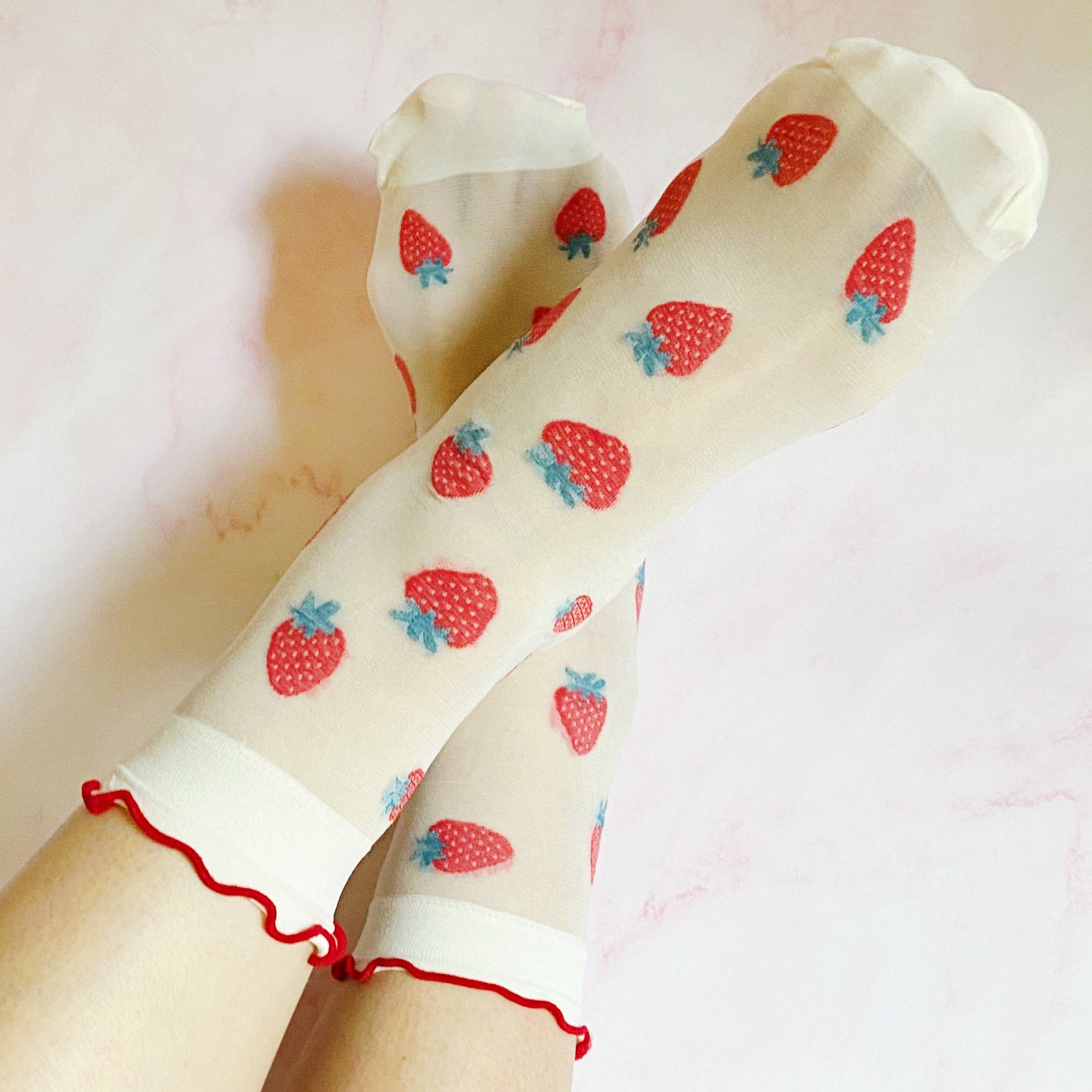 Sheer socks with strawberry pattern worn by a person on a light pink background