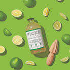 Glass cocktail bottle laying flat on green surface surrounded slices limes 