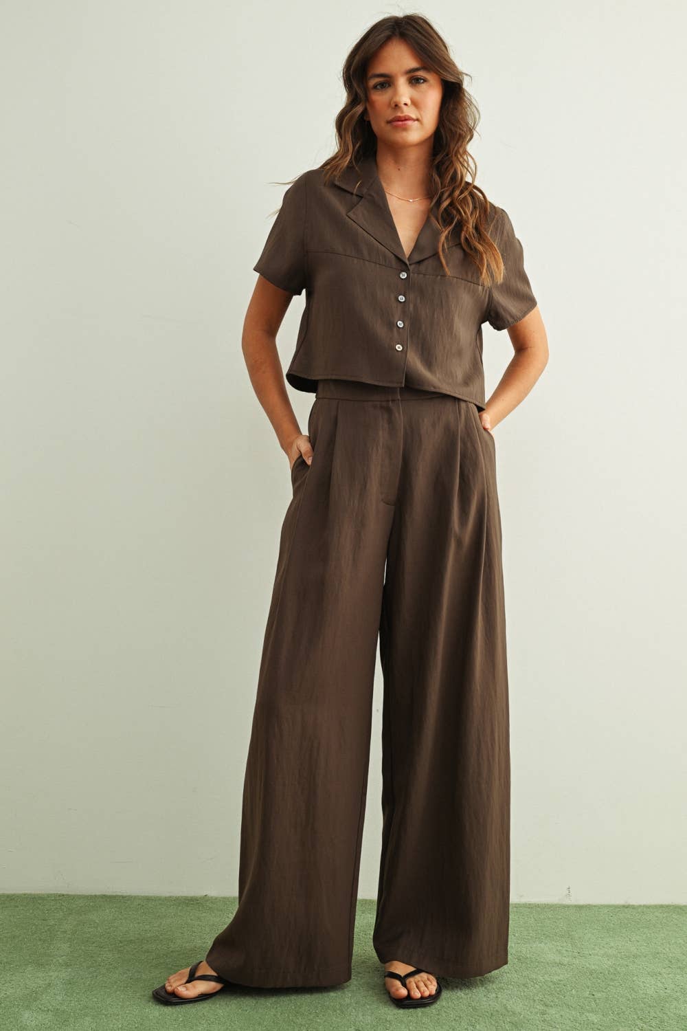 Woman wearing a brown outfit with wide-leg pants against a plain background
