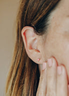 tiny pink heart-shaped opals set in a gold three-prong stud shown on close up of woman’s face and ear