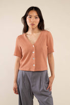 Woman wearing brick colored, ribbed, button down, short sleeve blouse top and grey pants 
