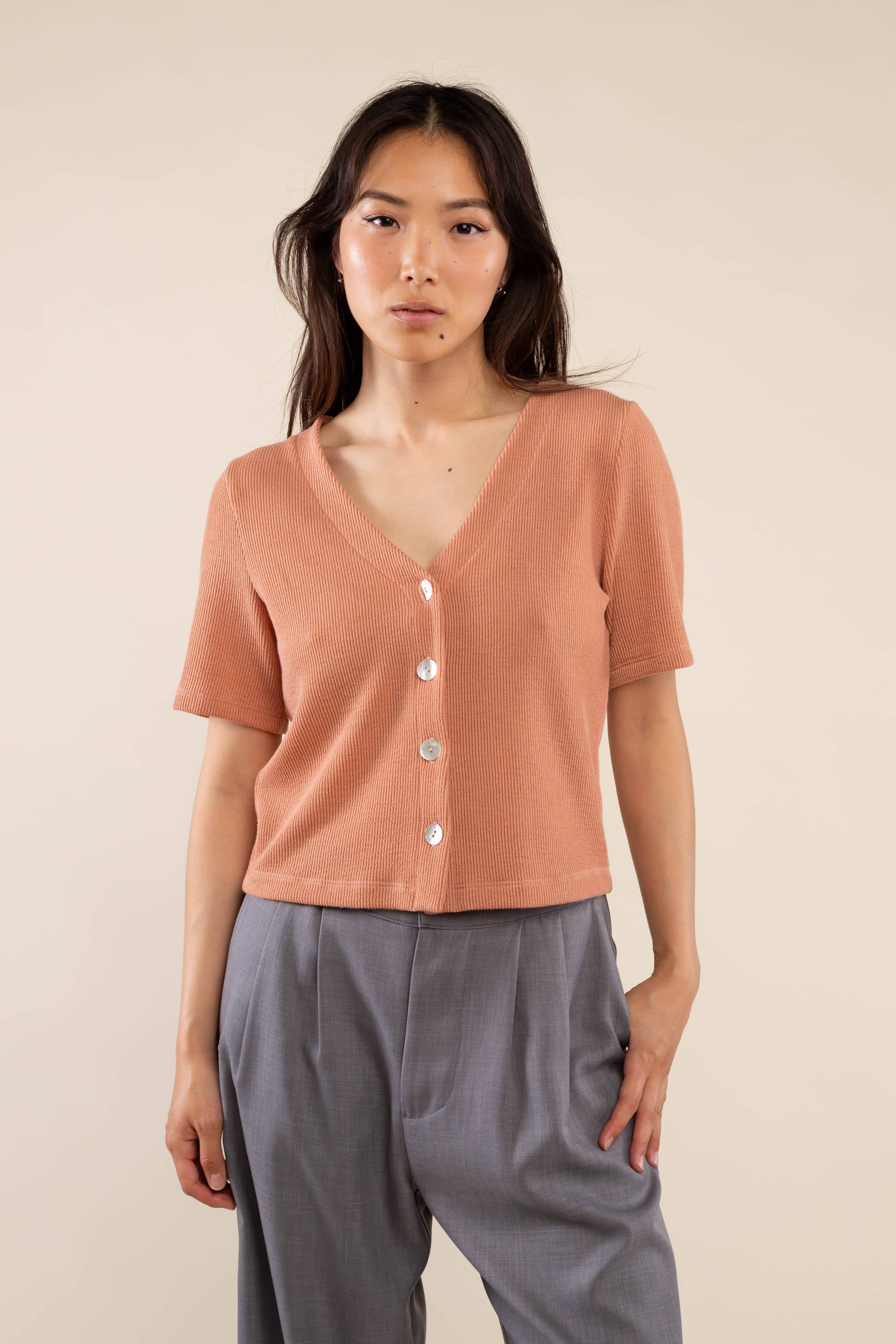 Woman wearing brick colored, ribbed, button down, short sleeve blouse top and grey pants 