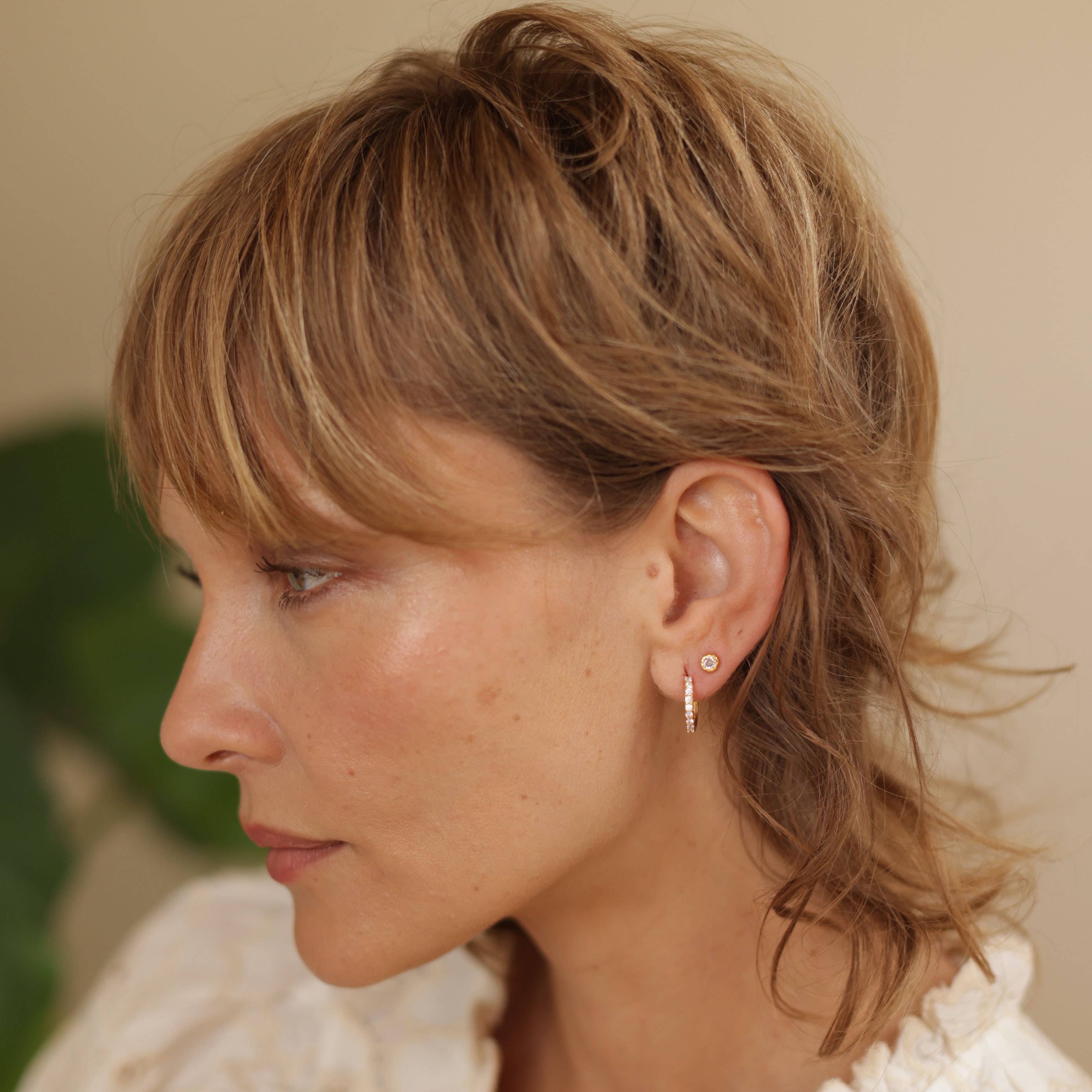 Woman with styled hair and earrings against a neutral background