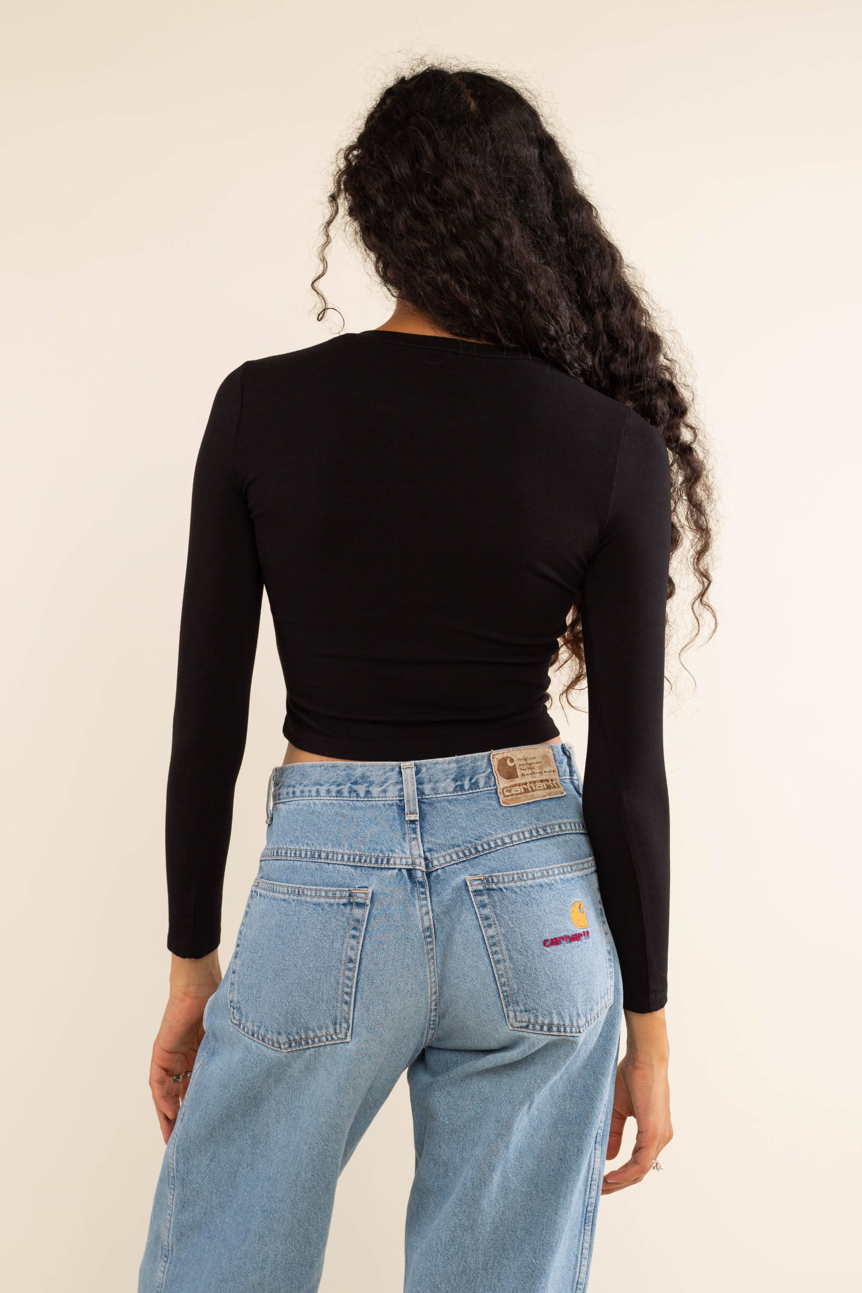 Woman wearing white, long sleeve, tight, crew neck, top with blue carhartt jeans