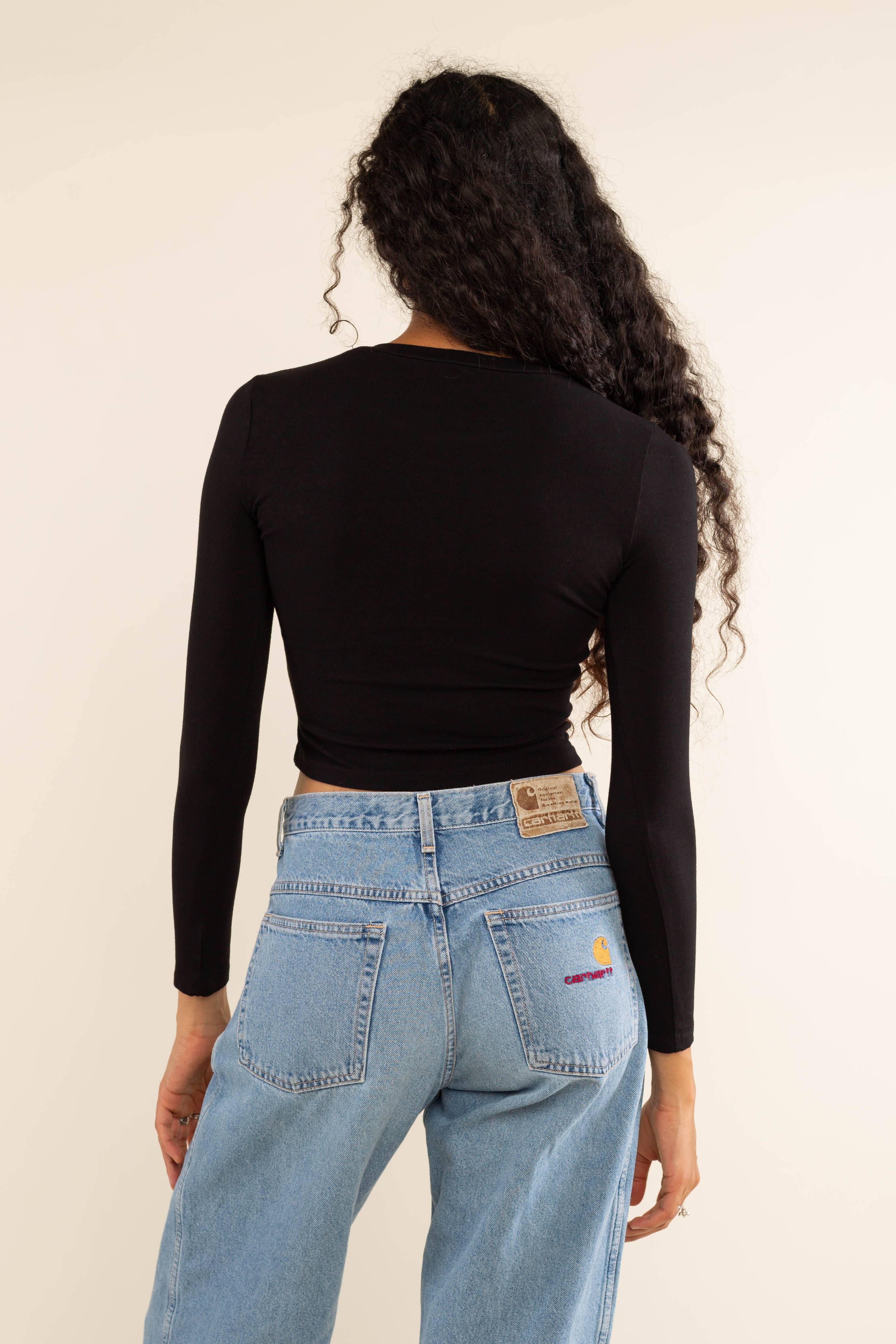 Woman wearing white, long sleeve, tight, crew neck, top with blue carhartt jeans