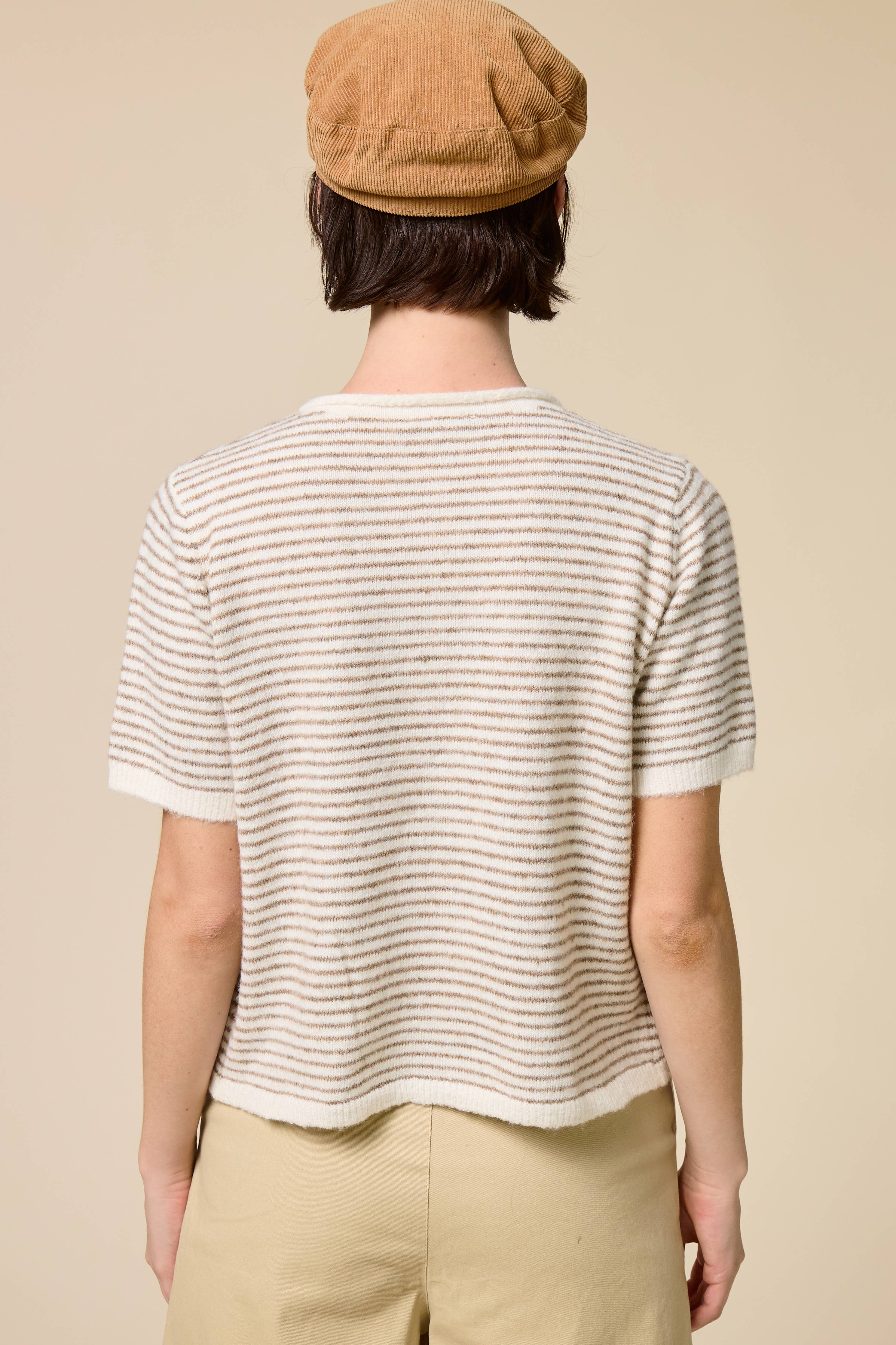 Person wearing a striped shirt and beige cap on a plain background