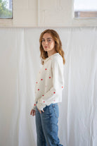 Woman wearing a cream cardigan with red hearts and buttons and blue jeans