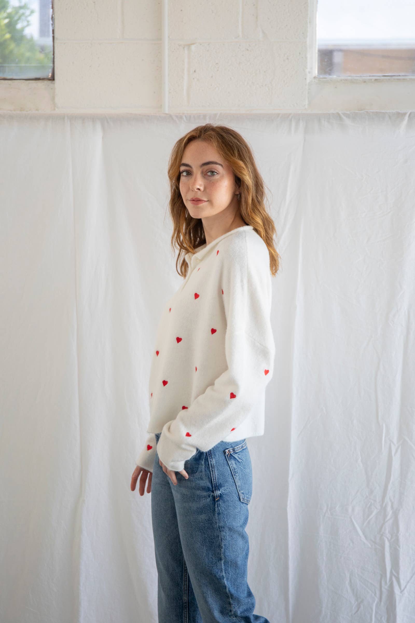 Woman wearing a cream cardigan with red hearts and buttons and blue jeans