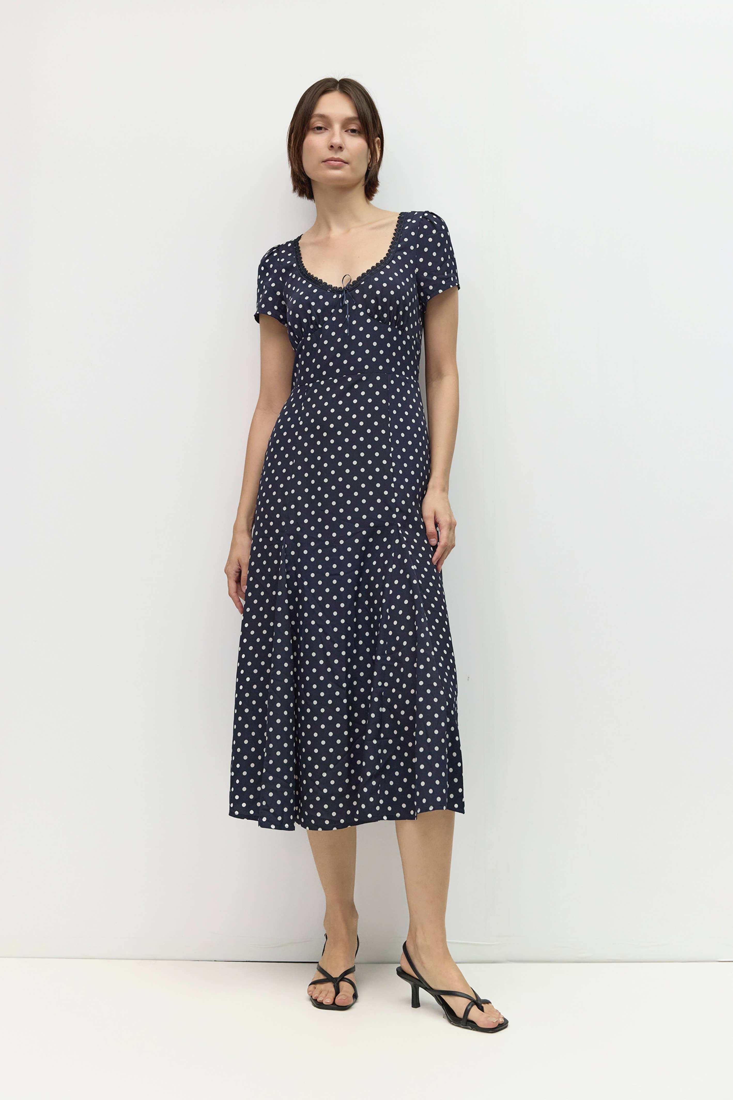 Woman wearing a navy dress with white polka dots against a white background