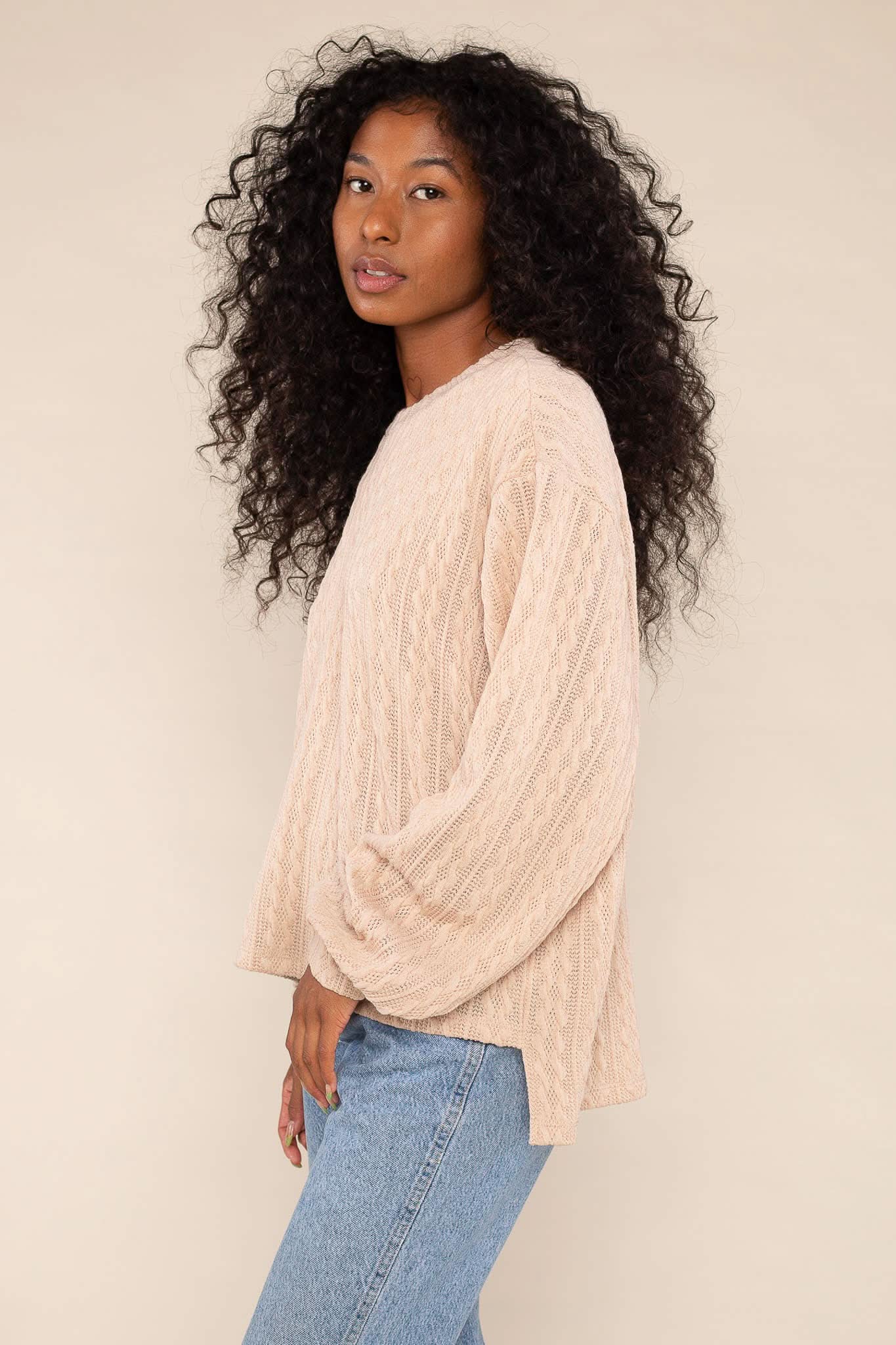 Woman wearing lightweight, beige, cable knit detail, sweater/ sweatshirt and blue jeans 