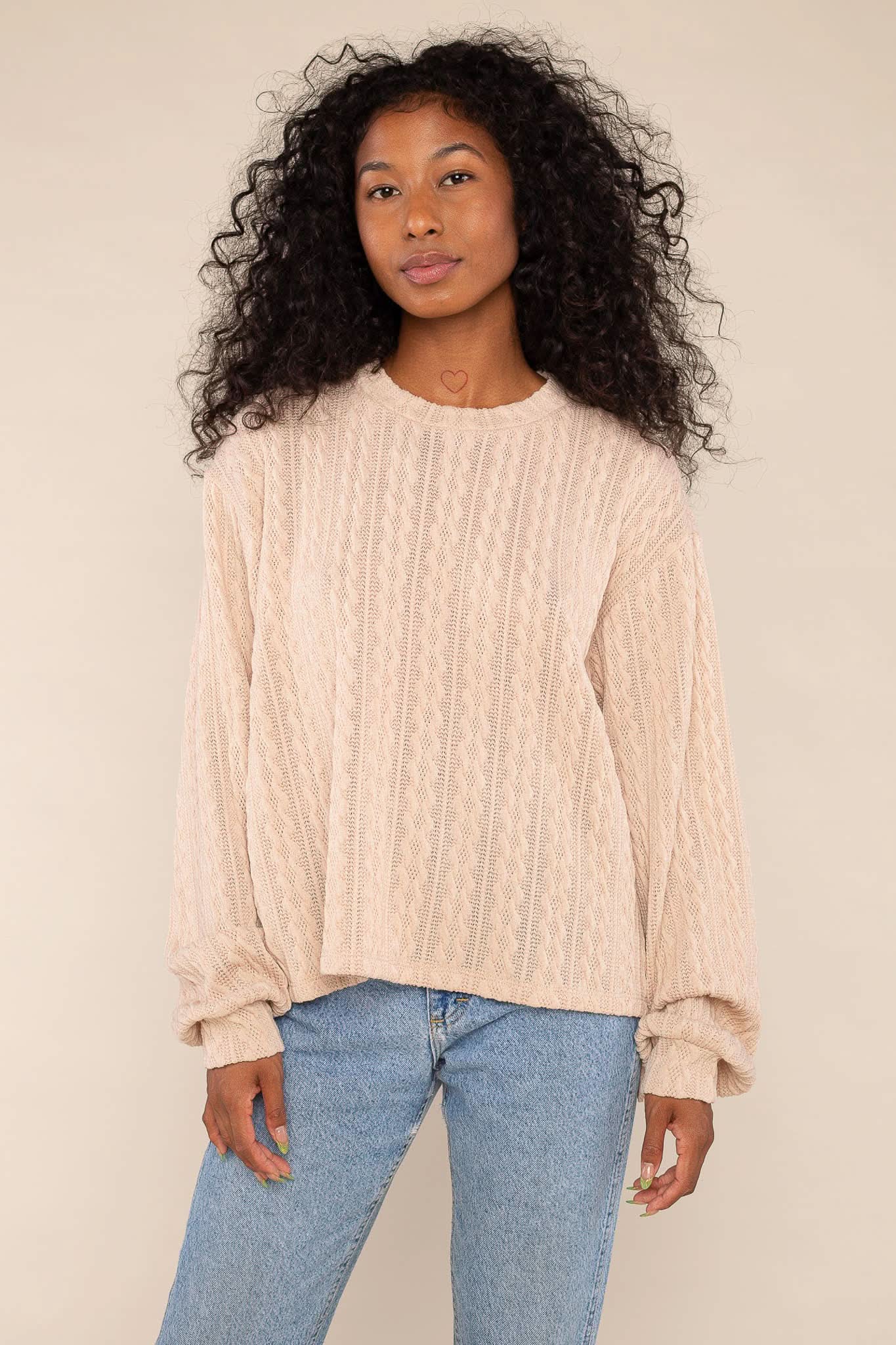 Woman wearing beige, cable knit detail, sweater/ sweatshirt and blue jeans 