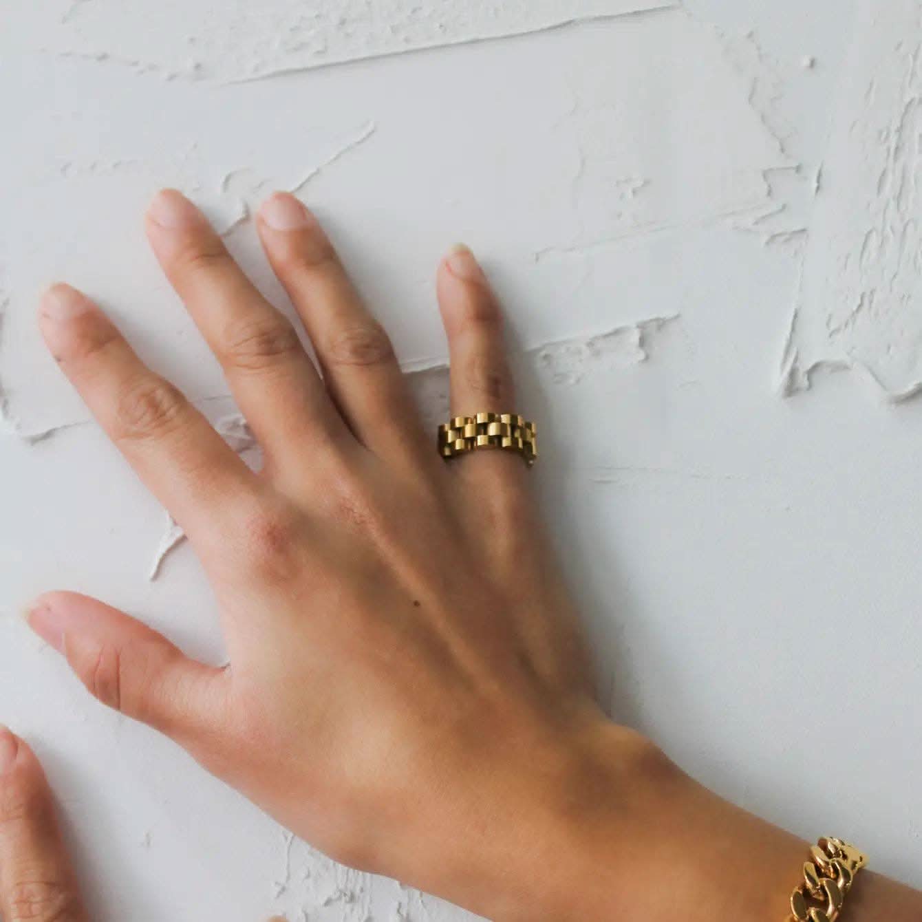 Hand wearing a gold ring on a textured white surface