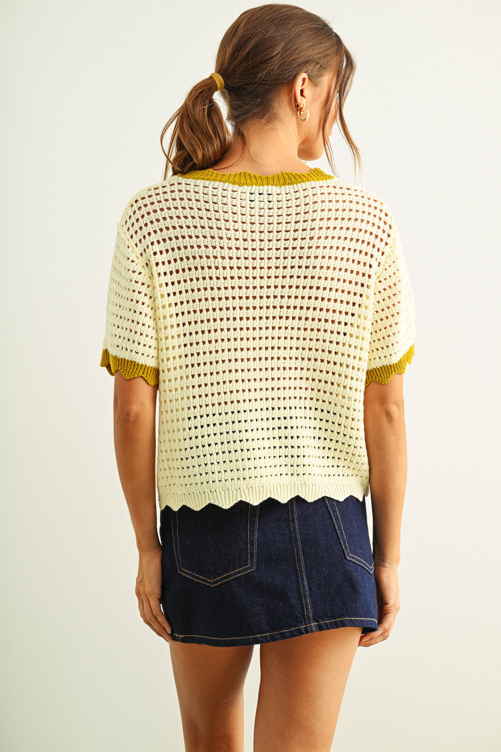 Woman wearing a white crochet top and denim skirt on a plain background