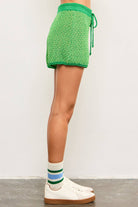 Woman wearing tube socks, tennis shoes, and green tie waist sweater shorts with dark green lining and light green and yellow details 