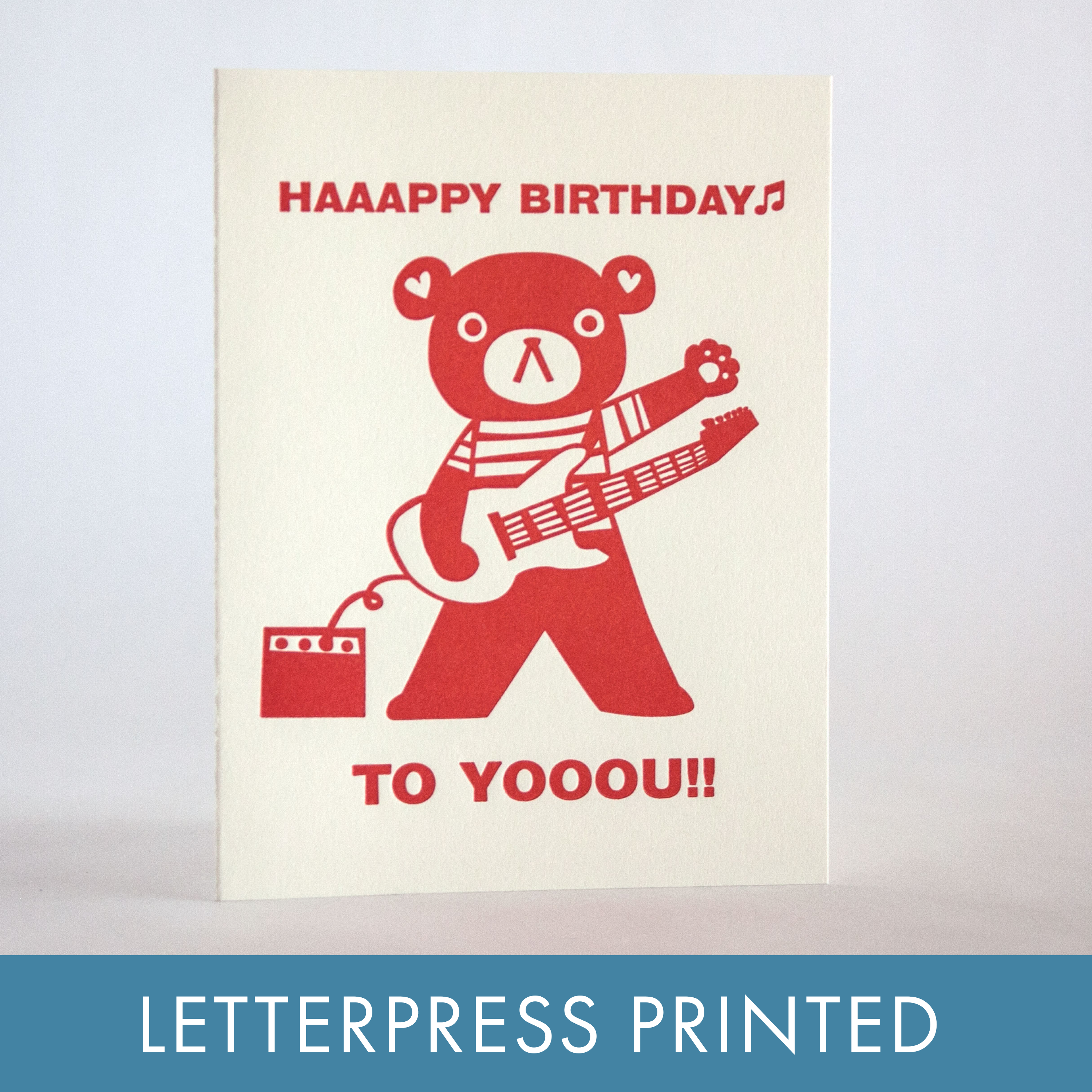 Letterpress printed birthday card with red bear playing guitar on a beige background