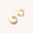 Gold ridged hoop earrings laying on a white background 