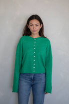Woman facing the camera wearing jeans and a dark Kelly green button up cardigan