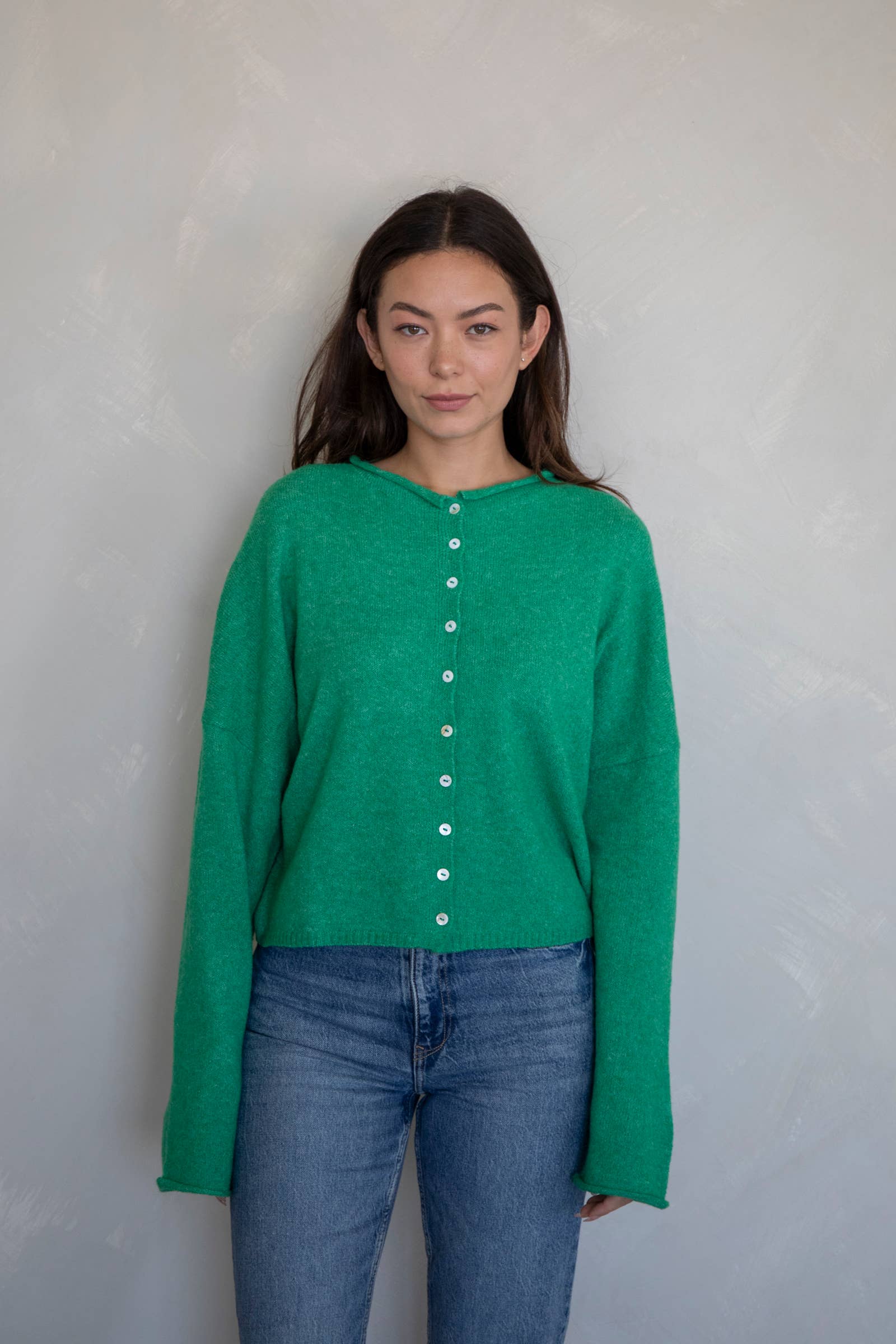 Woman facing the camera wearing jeans and a dark Kelly green button up cardigan