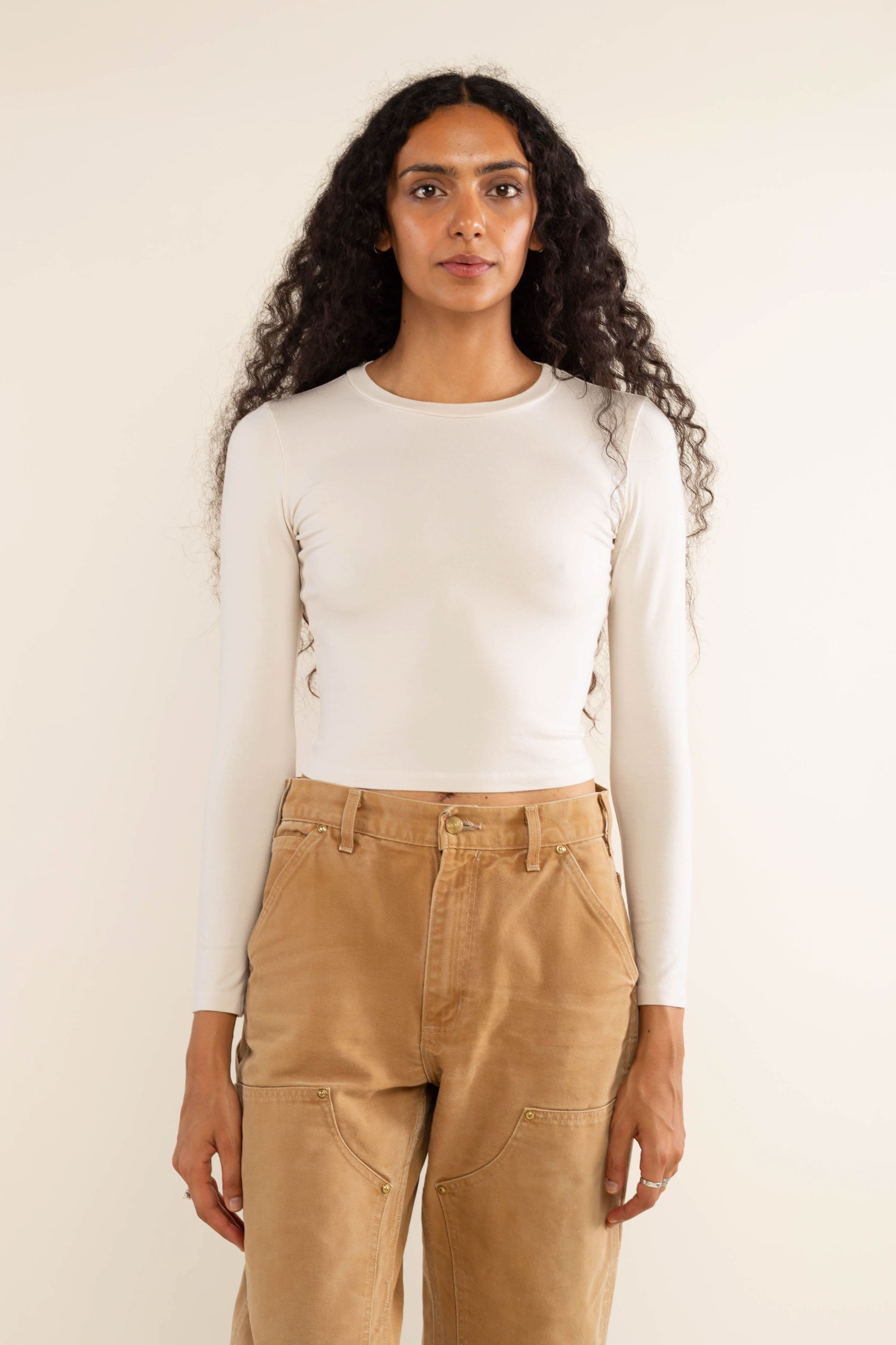 Woman wearing white, long sleeve, tight, crew neck, top with khaki jeans