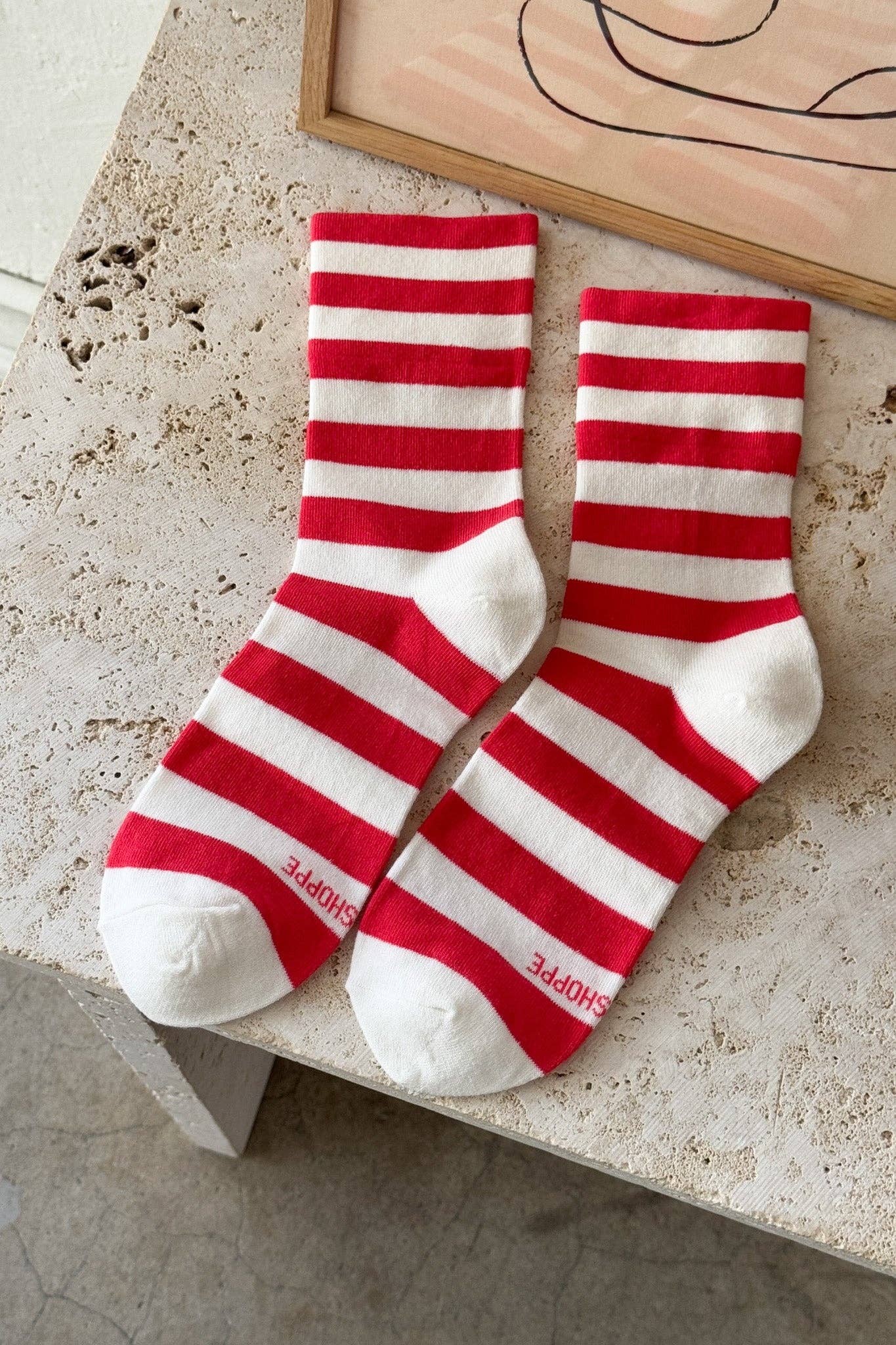 Red and white striped socks on a stone surface with a wooden frame in the background.