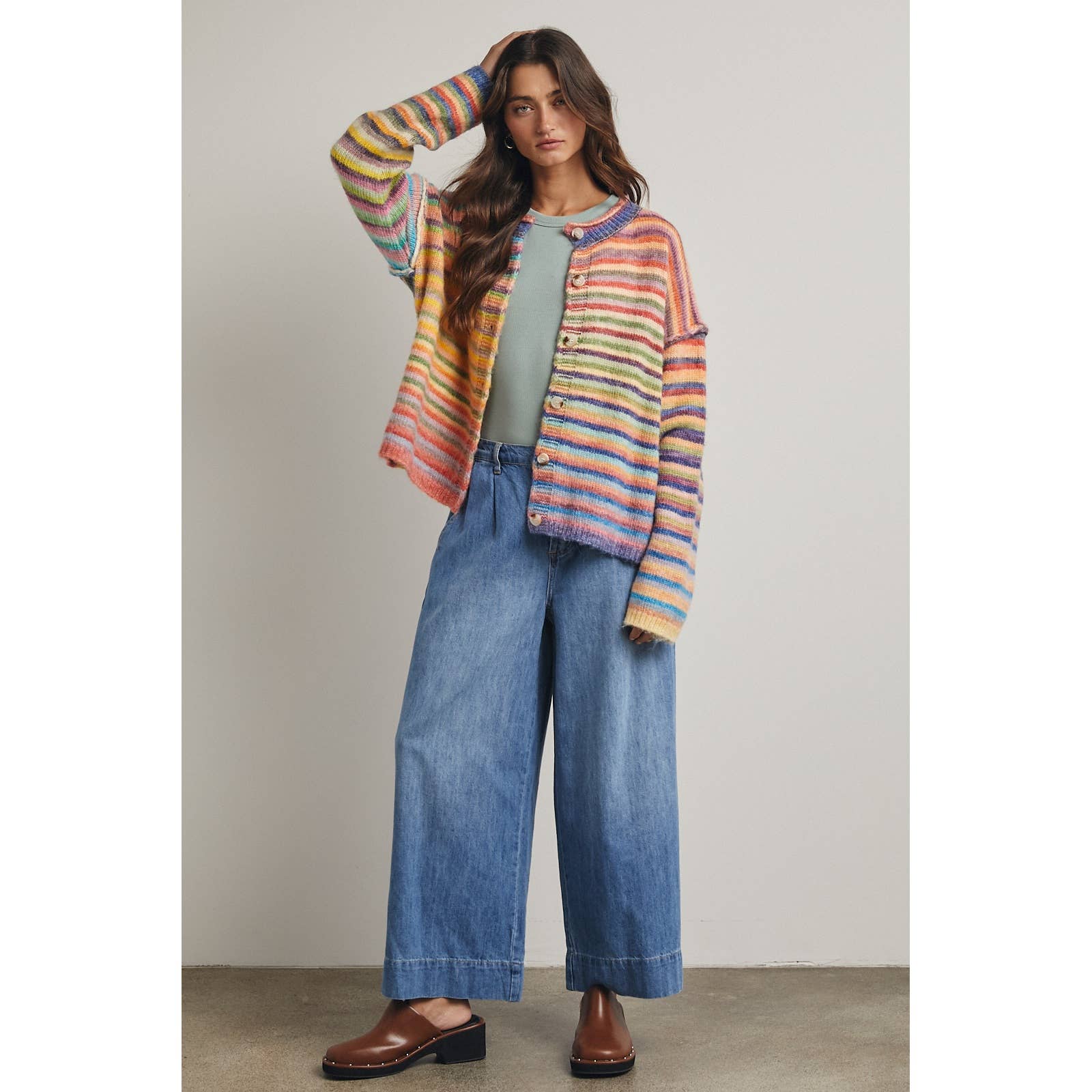 Woman wearing a colorful striped cardigan, green top, and blue jeans against a neutral background