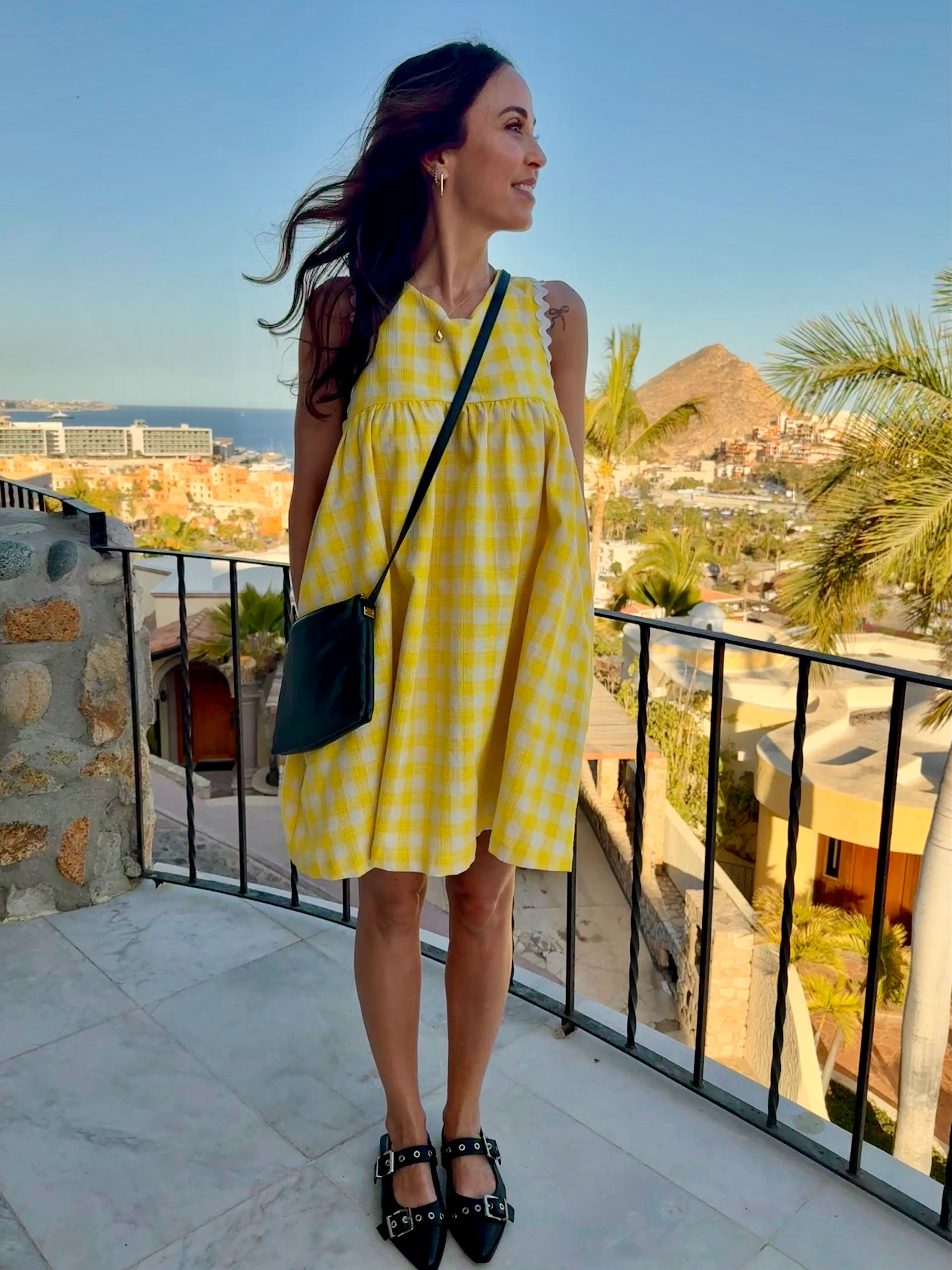 A woman wearing a yellow checkered mini dress with a sleeveless design, paired with black strappy sandals.