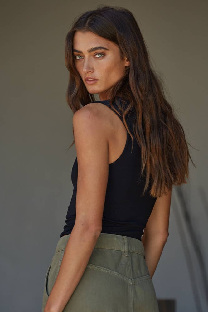Woman wearing a black sleeveless top and green pants against a neutral background