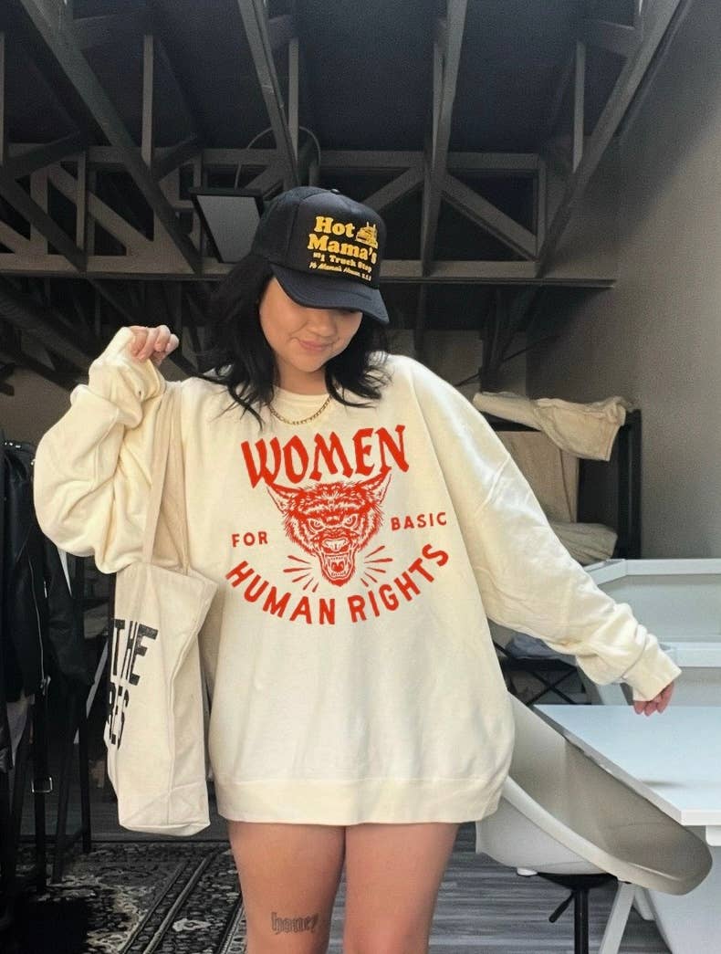 Person wearing a white sweatshirt with red text and a black cap in an indoor setting.