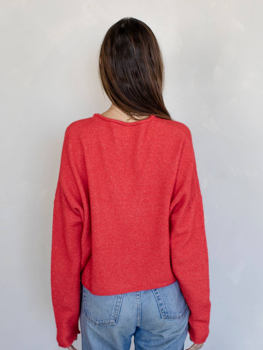 Woman smiling standing against white background wearing red button down cardigan with white buttons and blue jeans