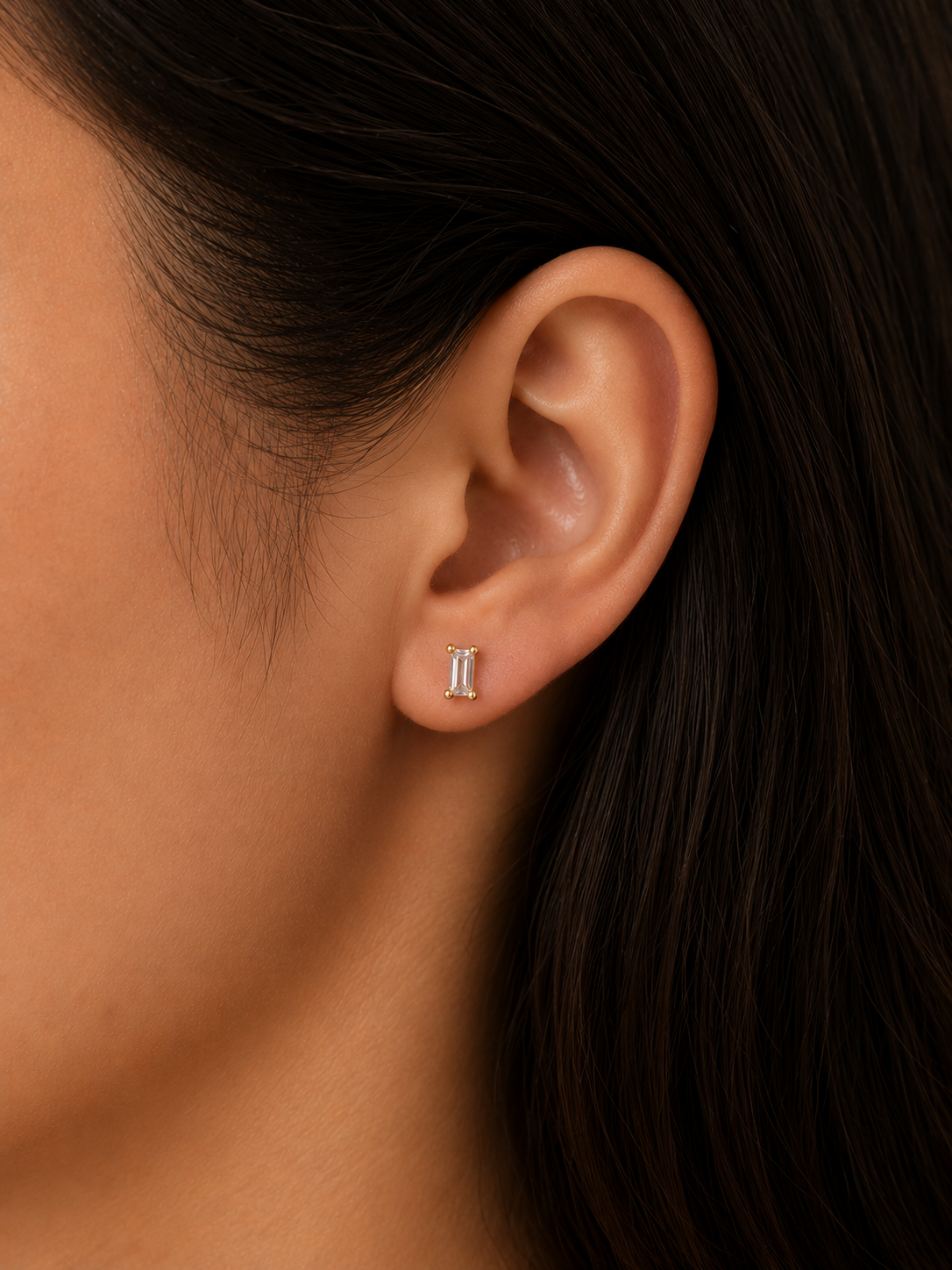 Close-up of an ear wearing a small earring with dark hair and skin background