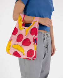 Model standing against White background holding BAGGU light pink reuse-able bag with apples and banana details  