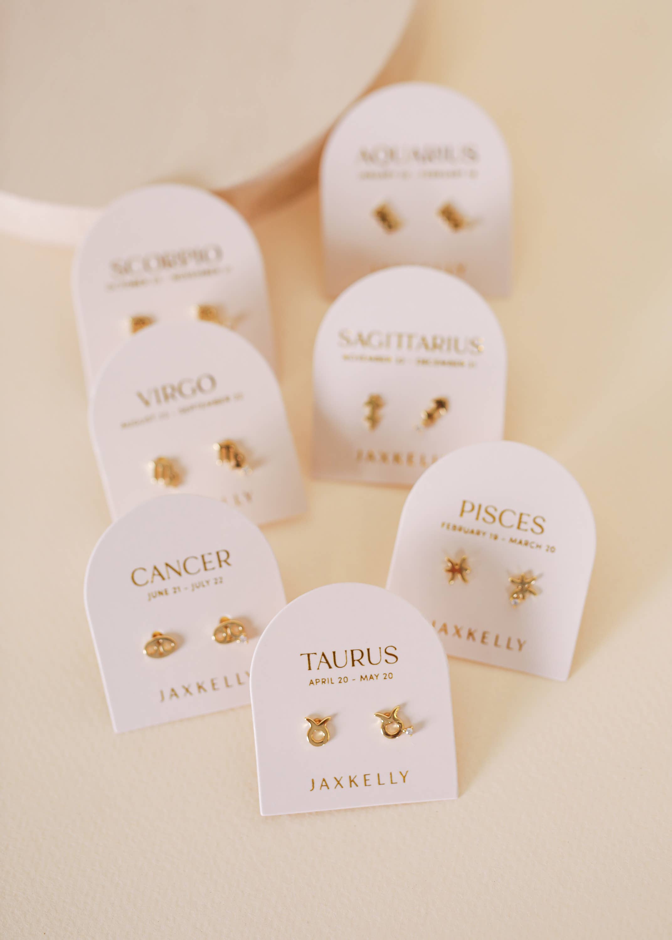 Gold zodiac charm studs in the shape of Aquarius, Taurus, Pisces, Virgo, Scorpio and Aquarius astrological signs. Each displayed on earring card a separate earring card