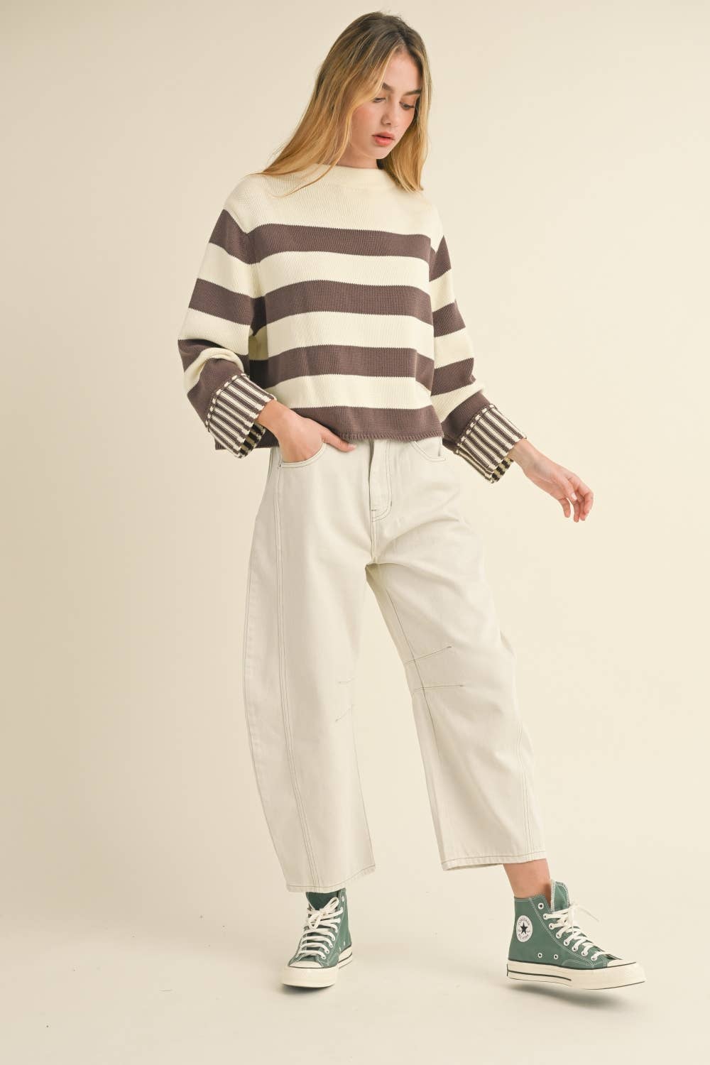 Woman wearing a striped sweater and white pants with green sneakers on a beige background