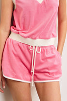 Woman wearing candy pink terry cloth towel shorts with white lining details and white drawstring with hand in pocket 