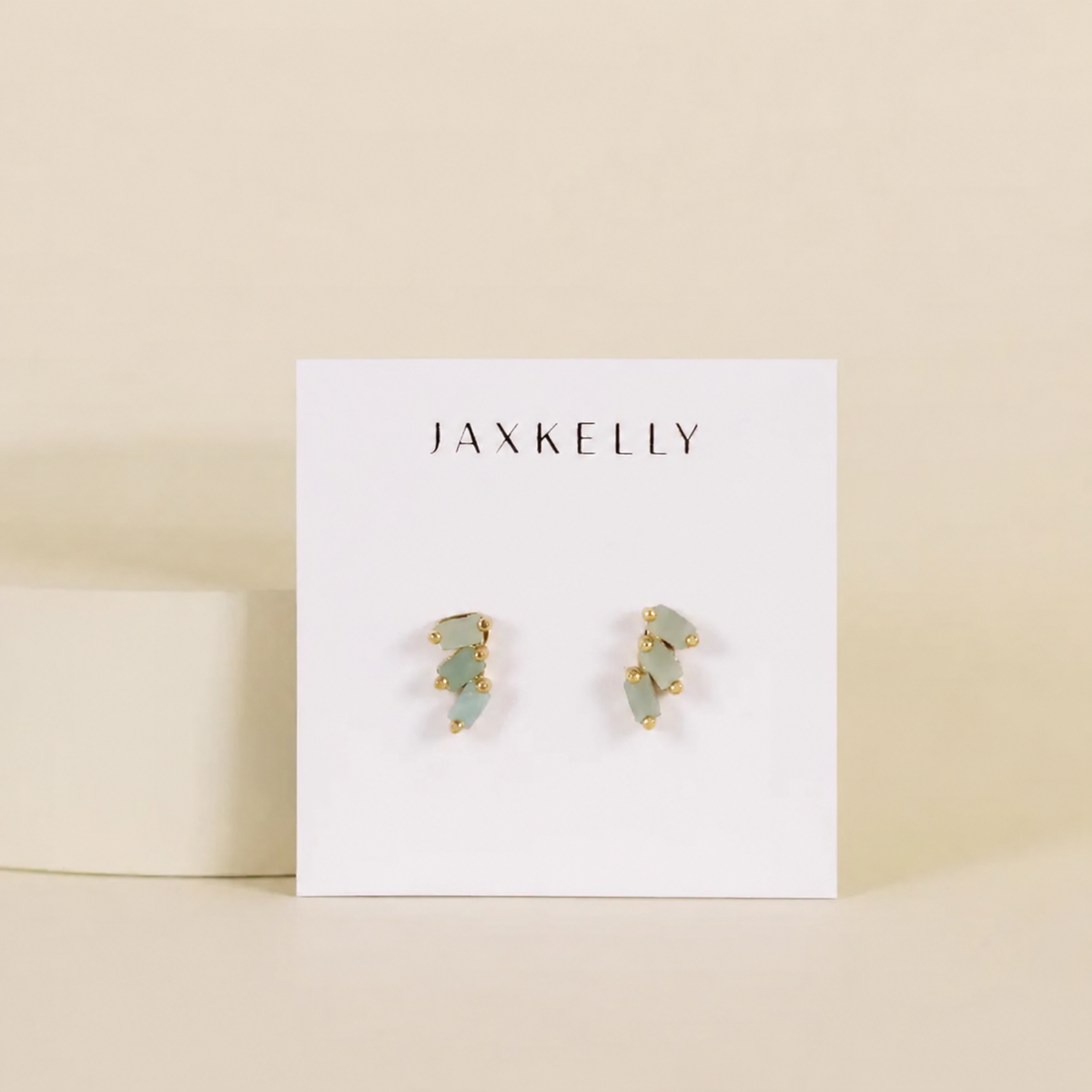 Pair of earrings on a Jaxkelly branded card against a beige background