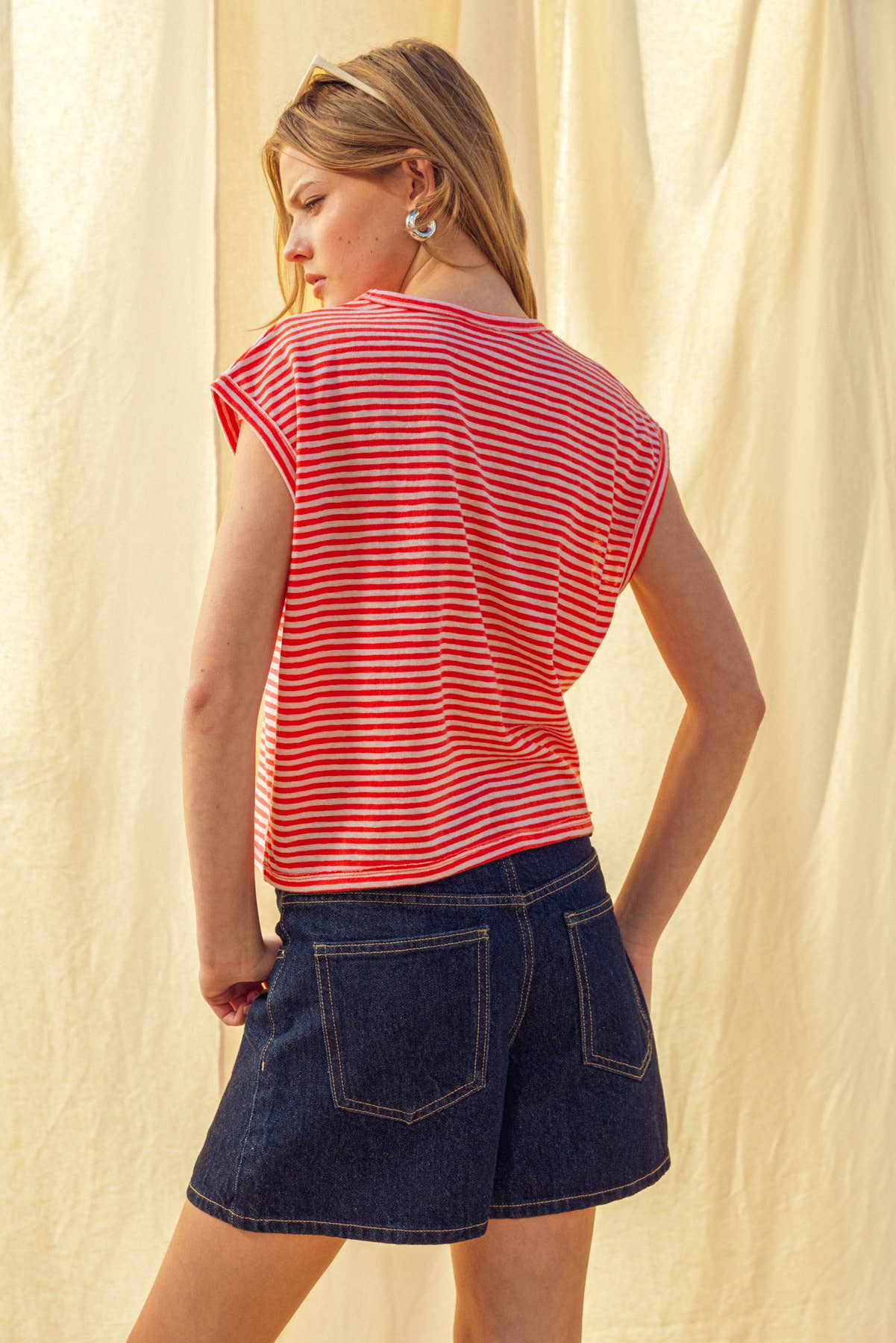 Woman wearing a red and white striped shirt with dark denim shorts against a light background