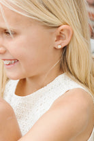 Child wearing Cute white cat with pink ears, flat back gold earrings laying on a white background 