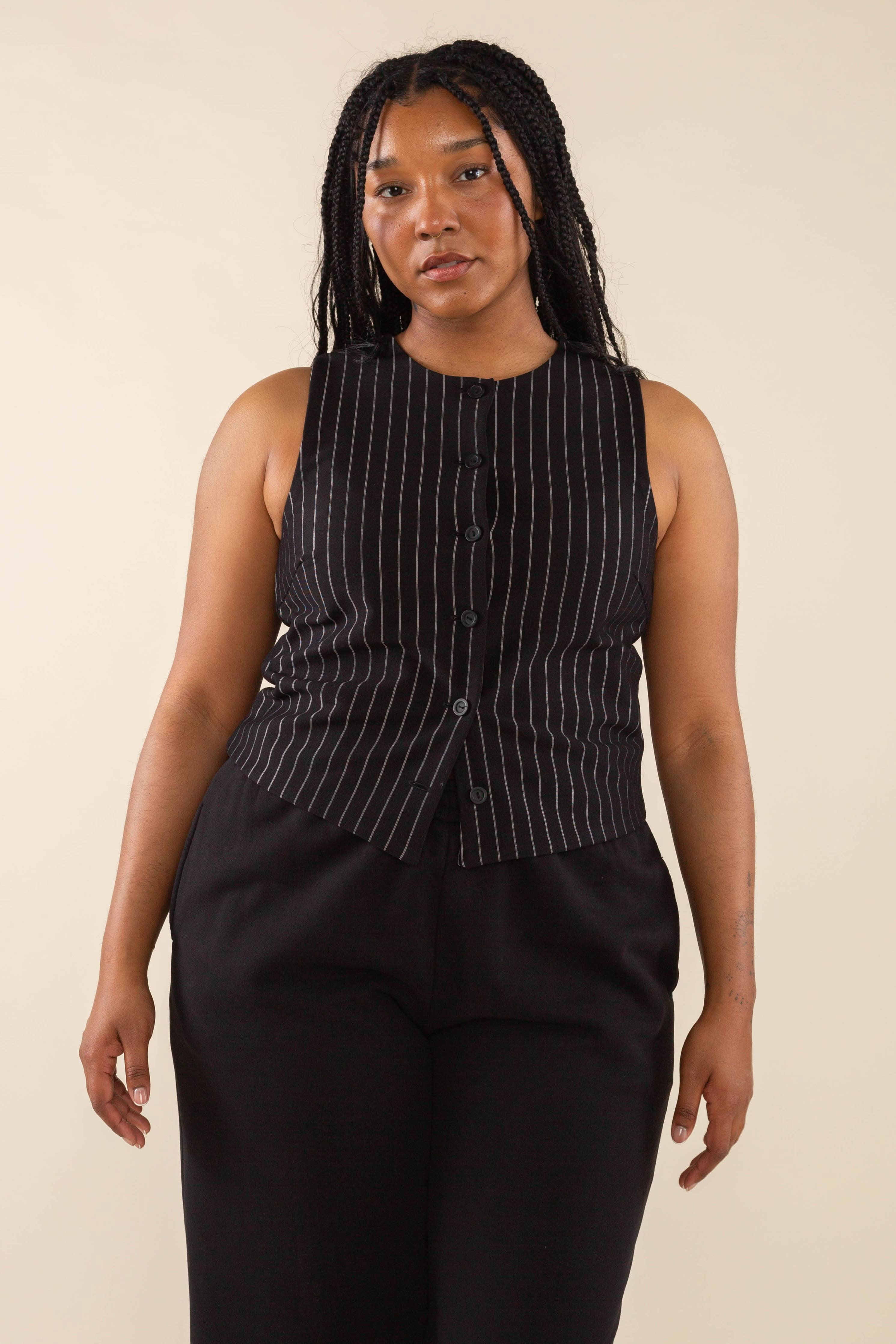 Woman wearing black high neck vest with cream pinstripes. Vest has black buttons all the way down 