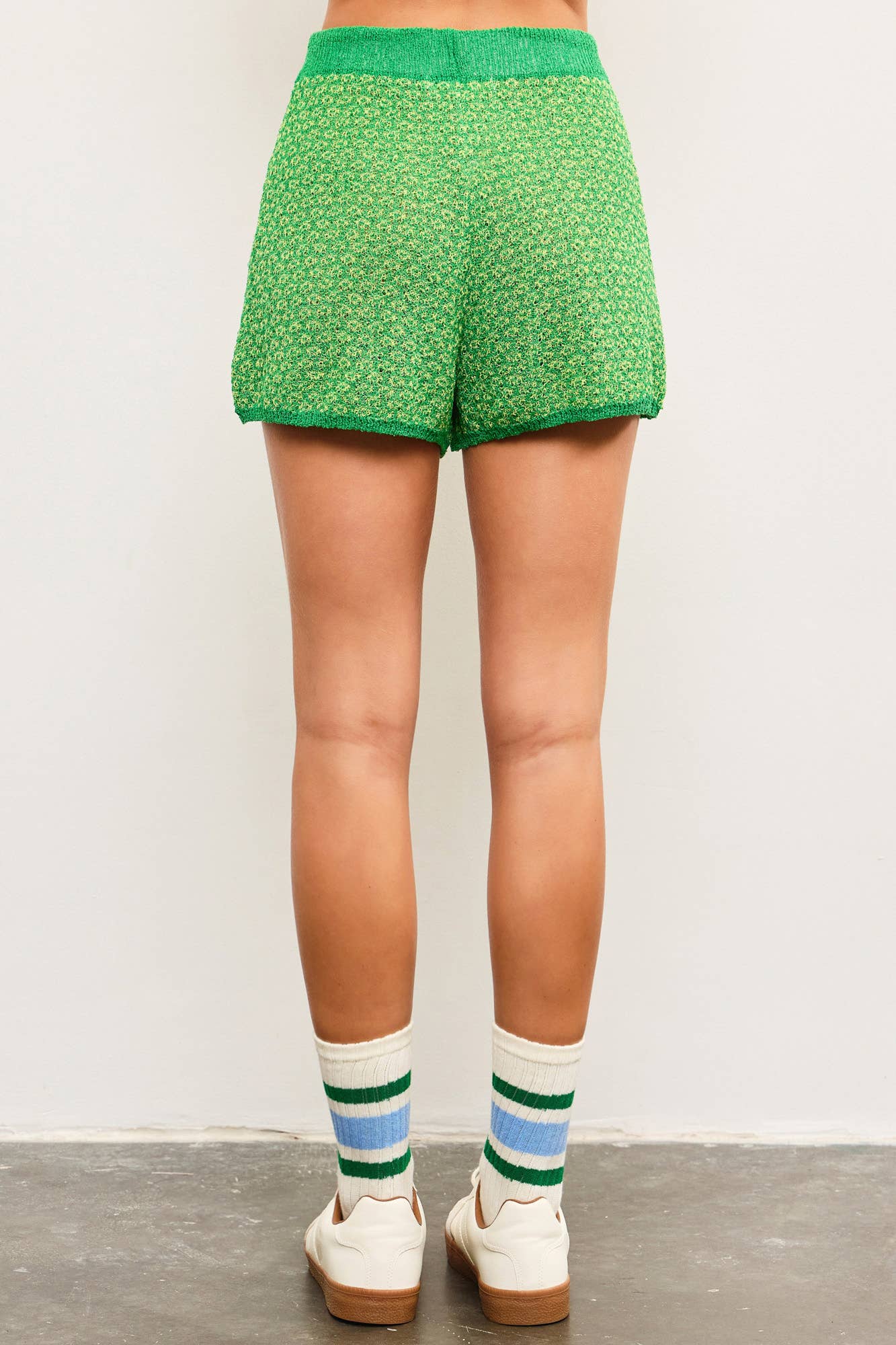 Woman wearing tube socks, tennis shoes, and green tie waist sweater shorts with dark green lining and light green and yellow details 