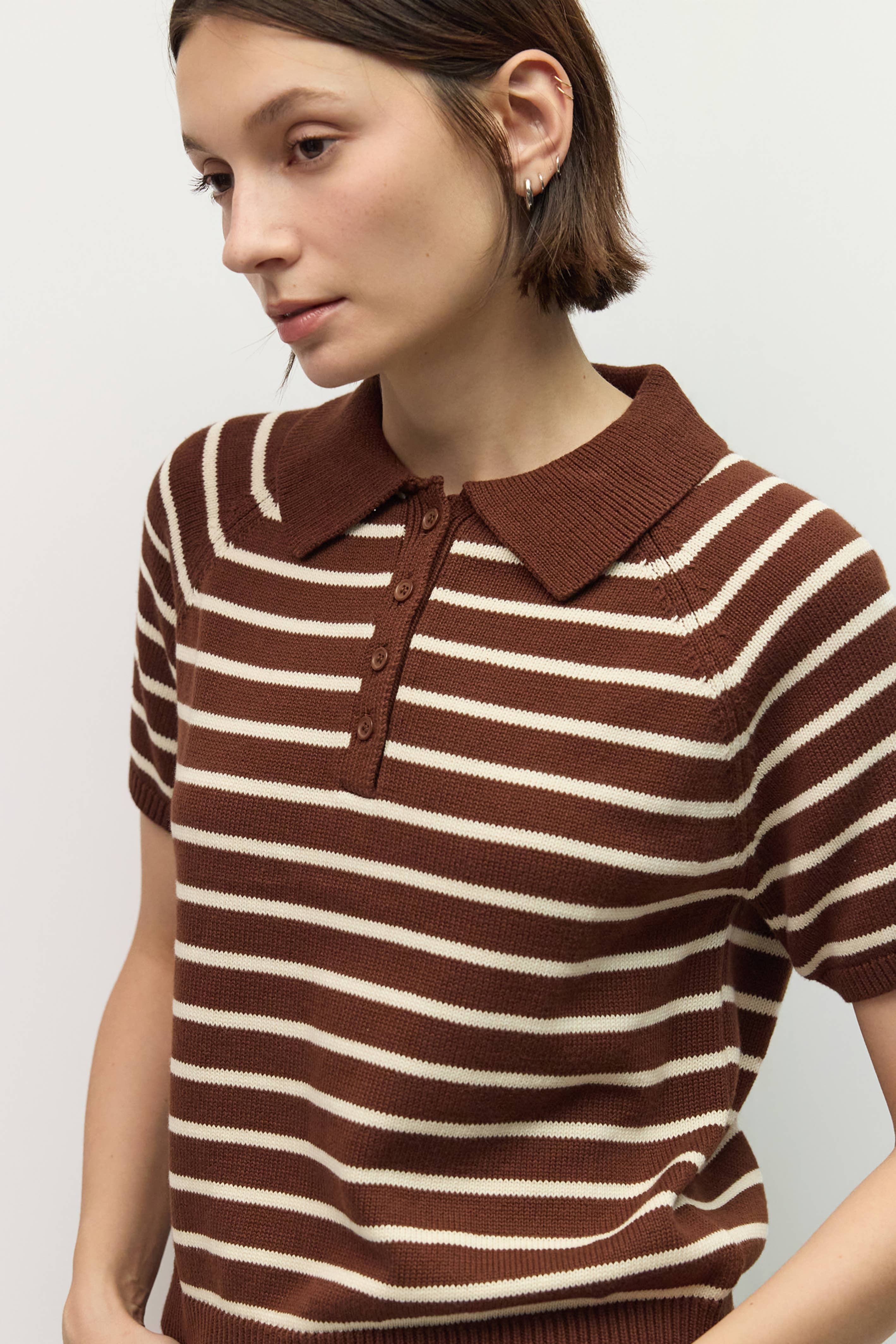 Woman wearing a brown and white striped sweater with a collar on a light gray background