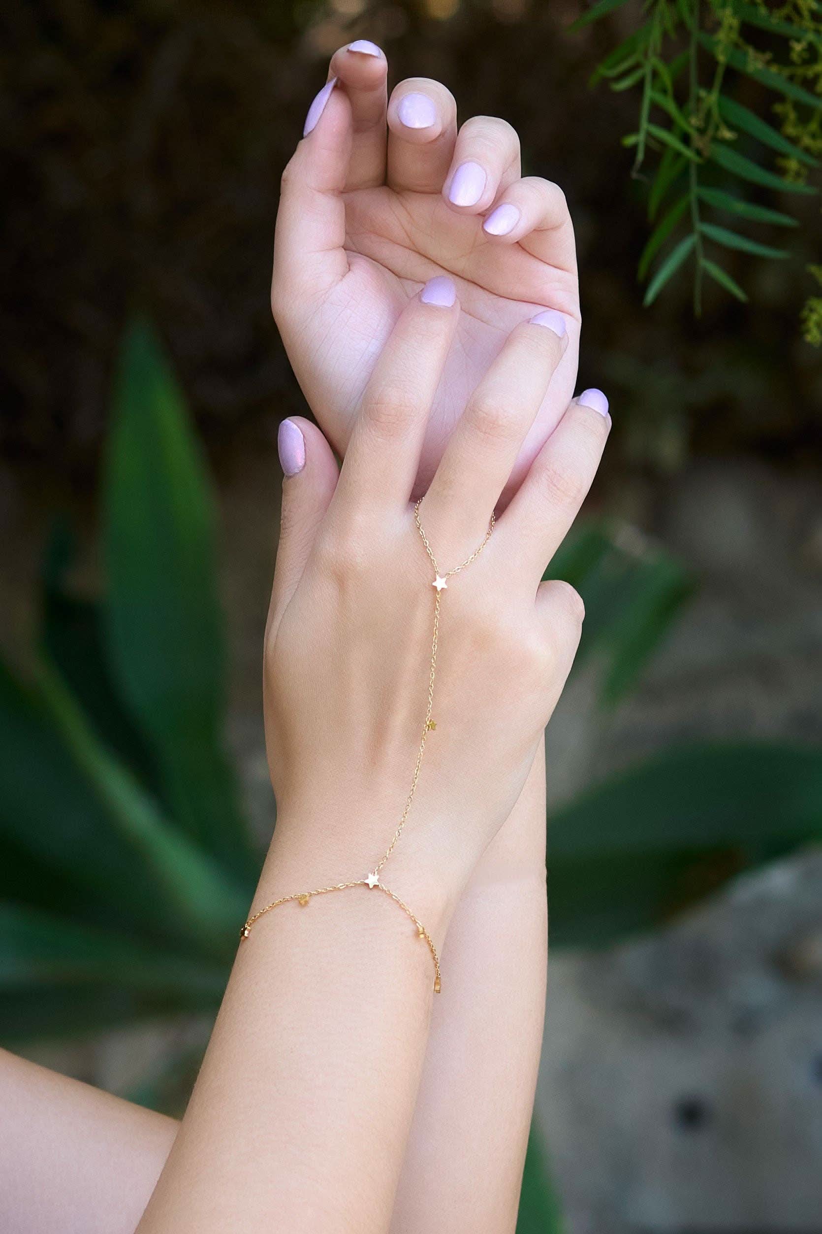 Hand wearing a delicate gold hand chain bracelet connected to a thin ring
