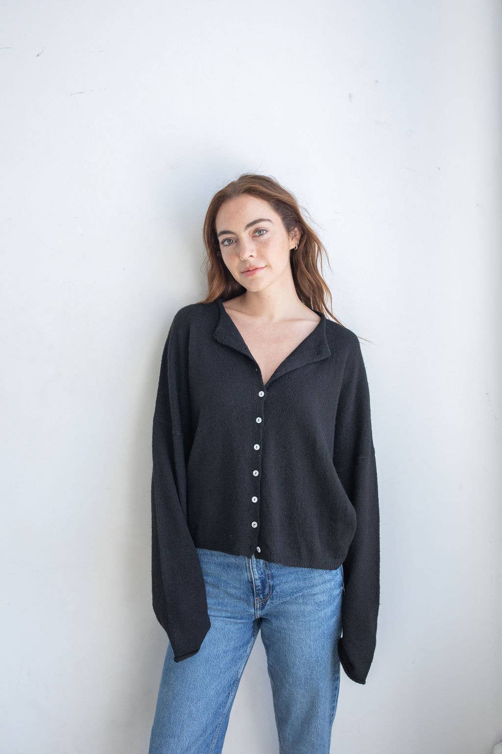 Woman wearing black cardigan with small white buttons and blue jeans 